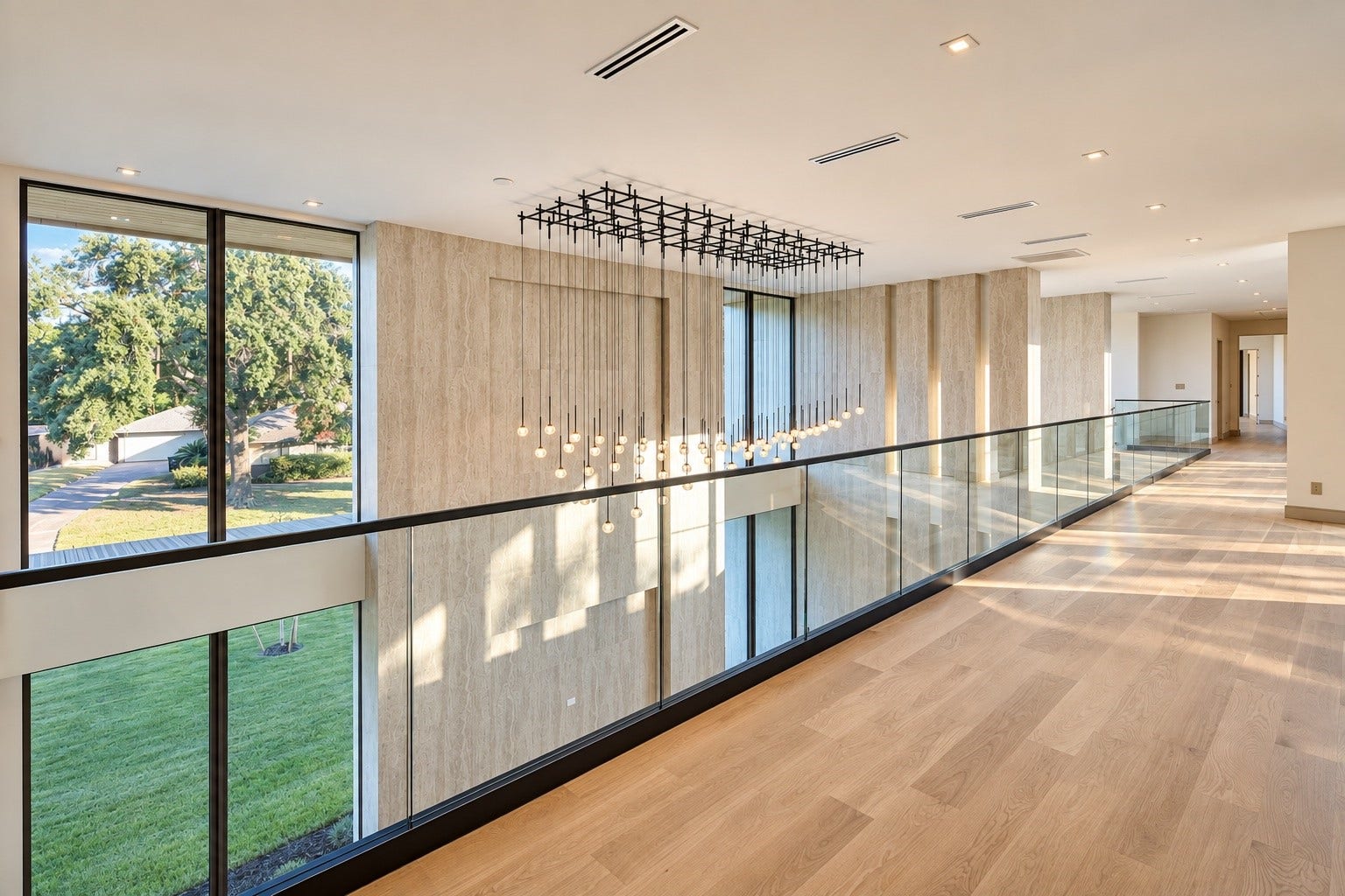 Architecture takes center stage in this alternate view of the second floor landing. Glass railing overlooks the spectacular living space below. Soaring windows, warm wood floors, stone surface and cascading light fixture come together in a striking composition . Every angle of this home was created to impress!