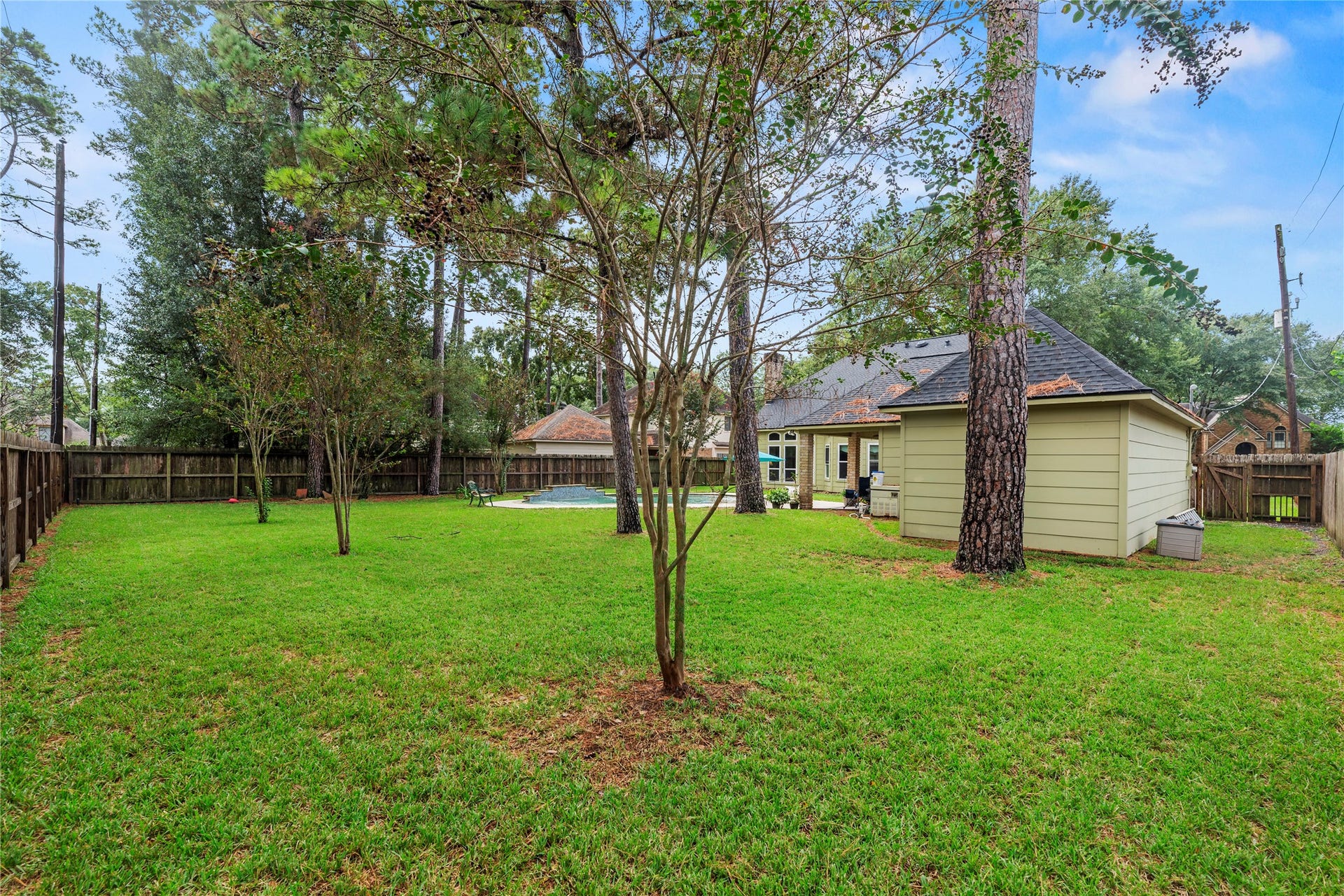 13114 S Winesap Lane, Cypress, TX 77429 Spacious fenced backyard with lush greenery, mature trees, a utility shed, and a patio area perfect for relaxation or entertaining.
