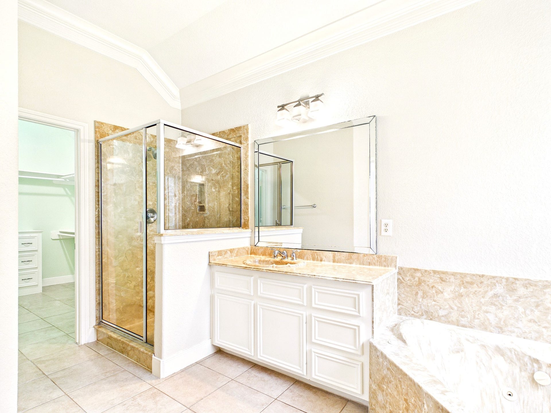 19521 Desna Drive, Porter, TX 77365 Bright and spacious primary bathroom featuring a glass-enclosed shower, a large mirror above a white vanity, and a luxurious bathtub with marble-like accents. The room is well-lit with modern fixtures and has a clean, elegant design.