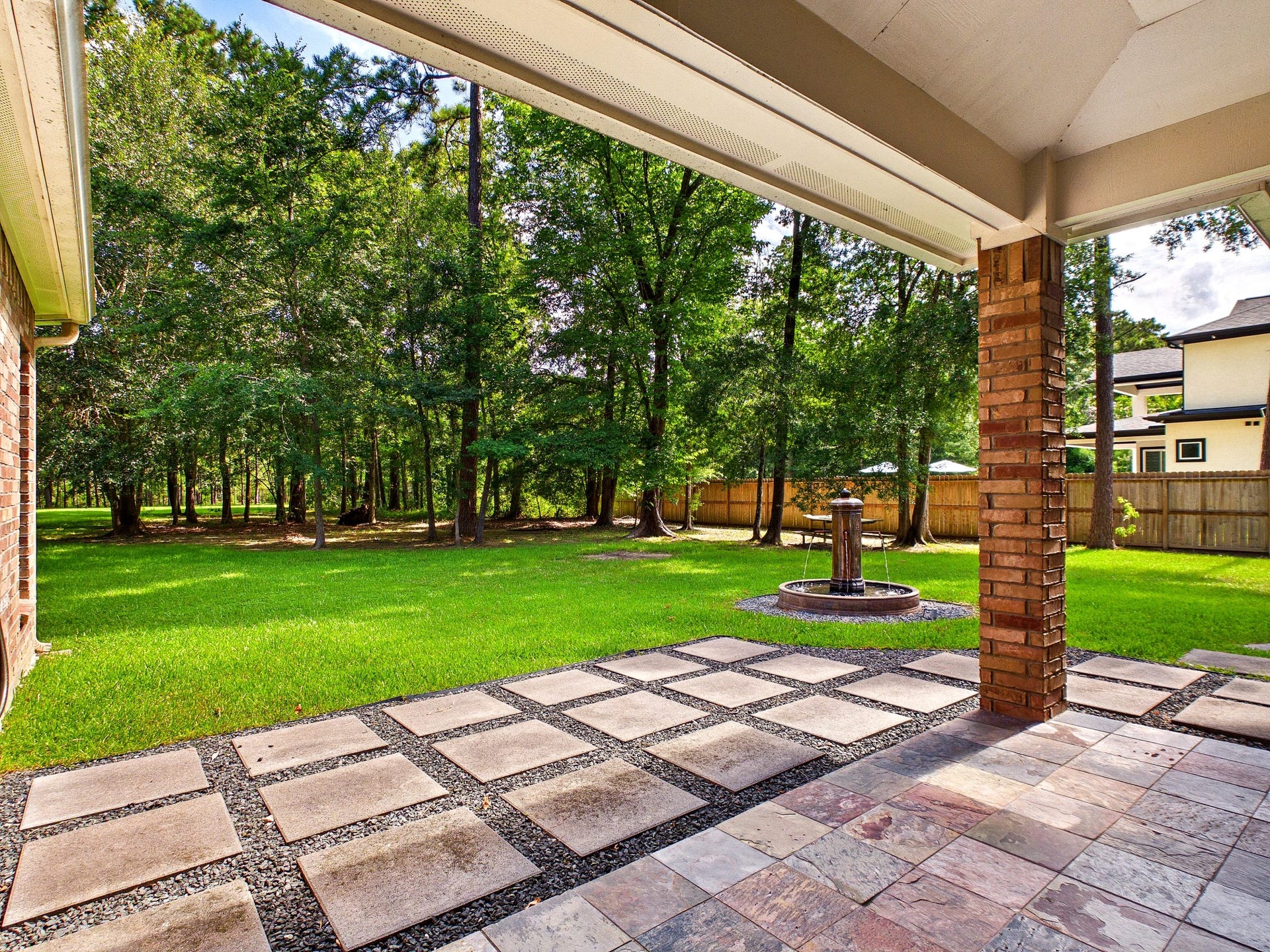 19521 Desna Drive, Porter, TX 77365 Spacious backyard with a patio featuring stone tiles and a fountain, surrounded by lush greenery and is fully fenced for privacy. Ideal for outdoor relaxation and entertaining.