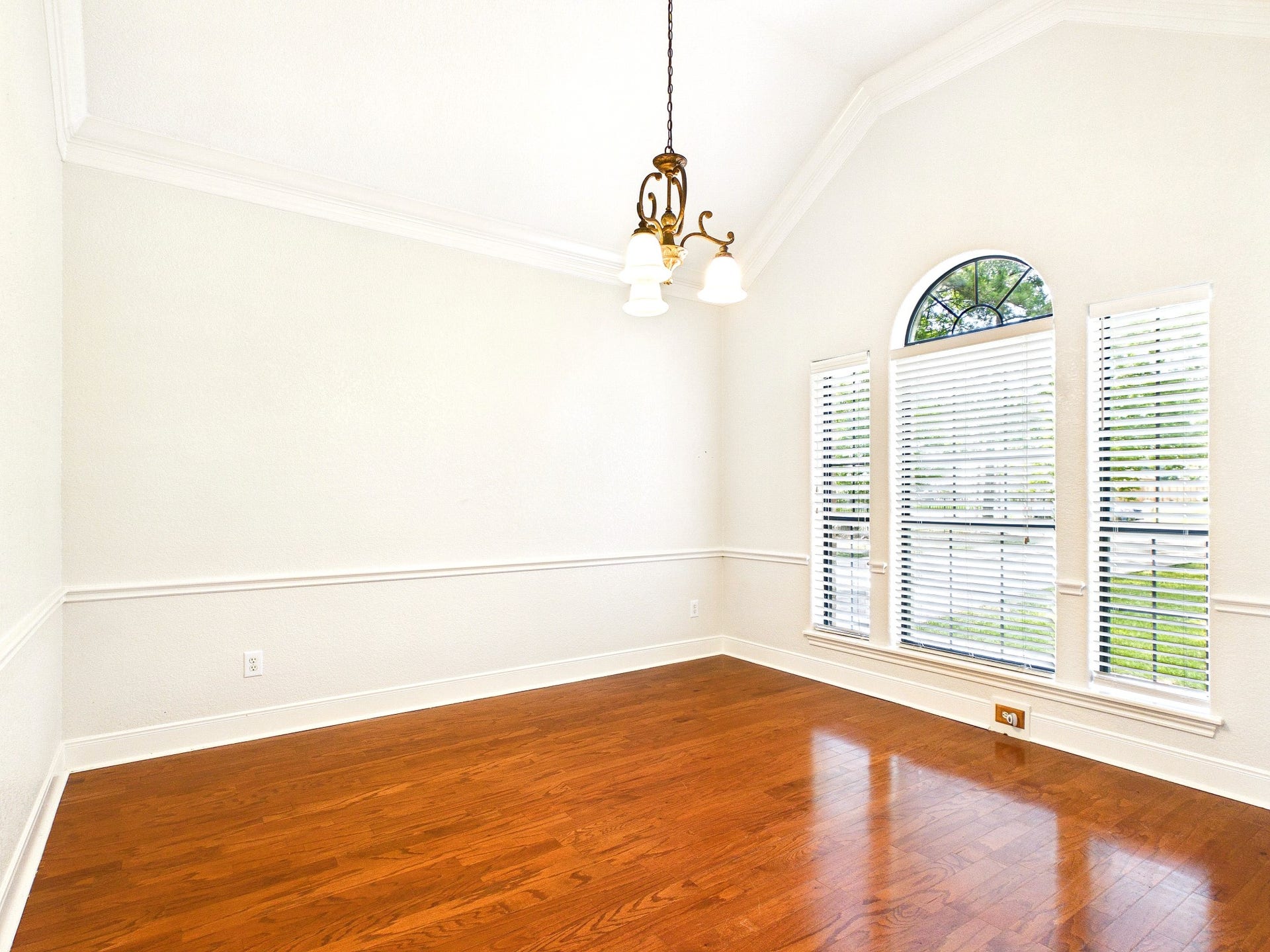 19521 Desna Drive, Porter, TX 77365 This bright dining room features a vaulted ceiling, elegant light fixture, and large arched windows with blinds, showcasing beautiful hardwood floors and fresh neutral paint.