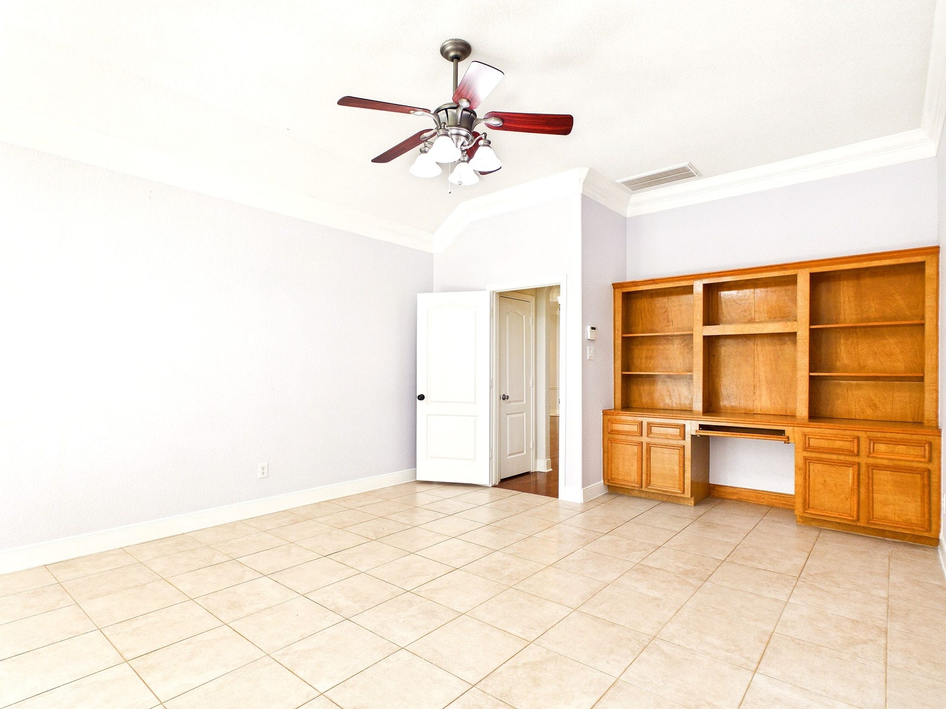 19521 Desna Drive, Porter, TX 77365 This bright primary bedroom features tiled flooring, a ceiling fan, and built-in wooden shelves, offering ample storage and a clean, open space.