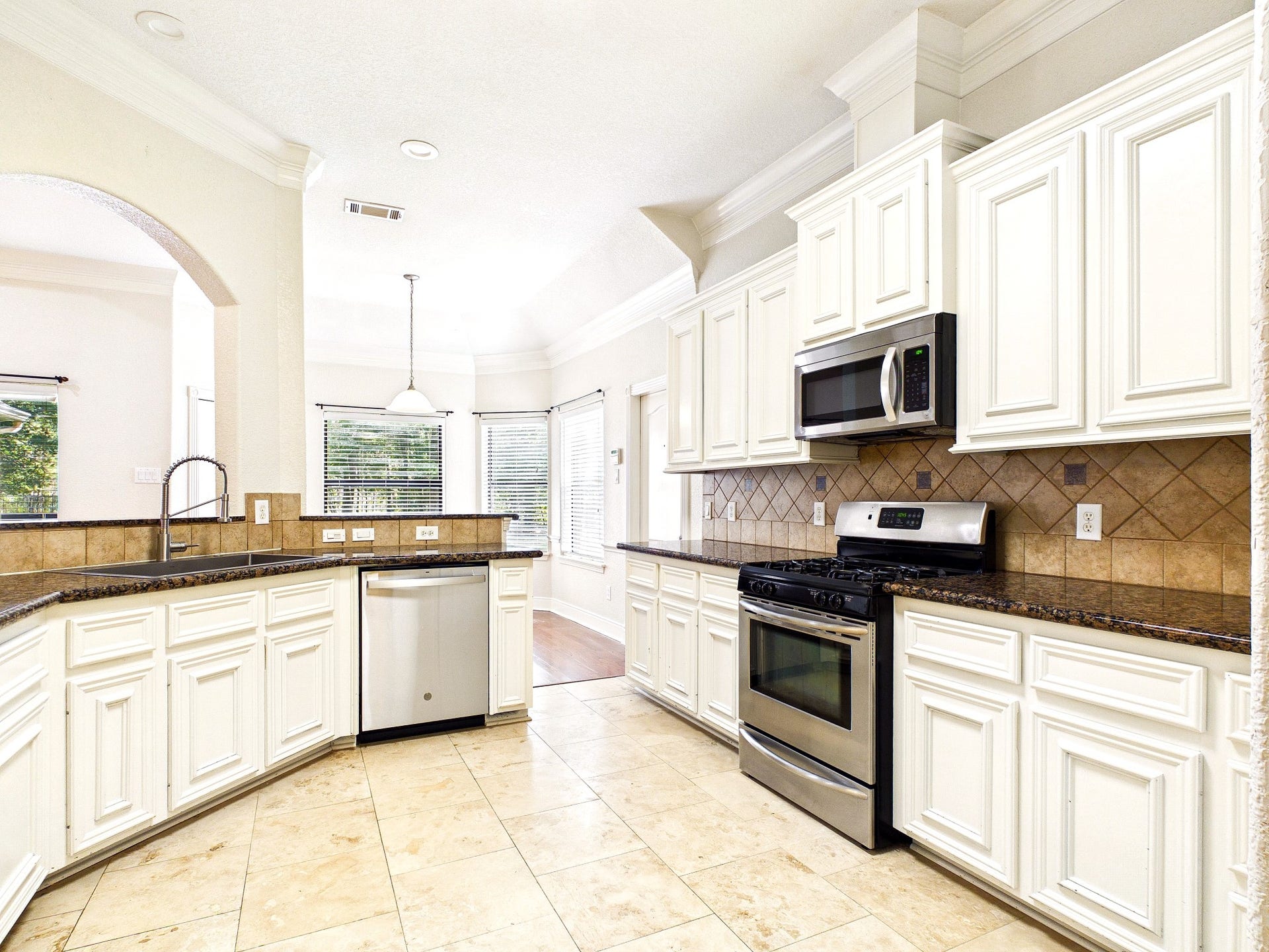 19521 Desna Drive, Porter, TX 77365 Bright, spacious kitchen with white cabinetry, stainless steel appliances, and a tile backsplash. The room features a large window for natural light and a convenient open layout.