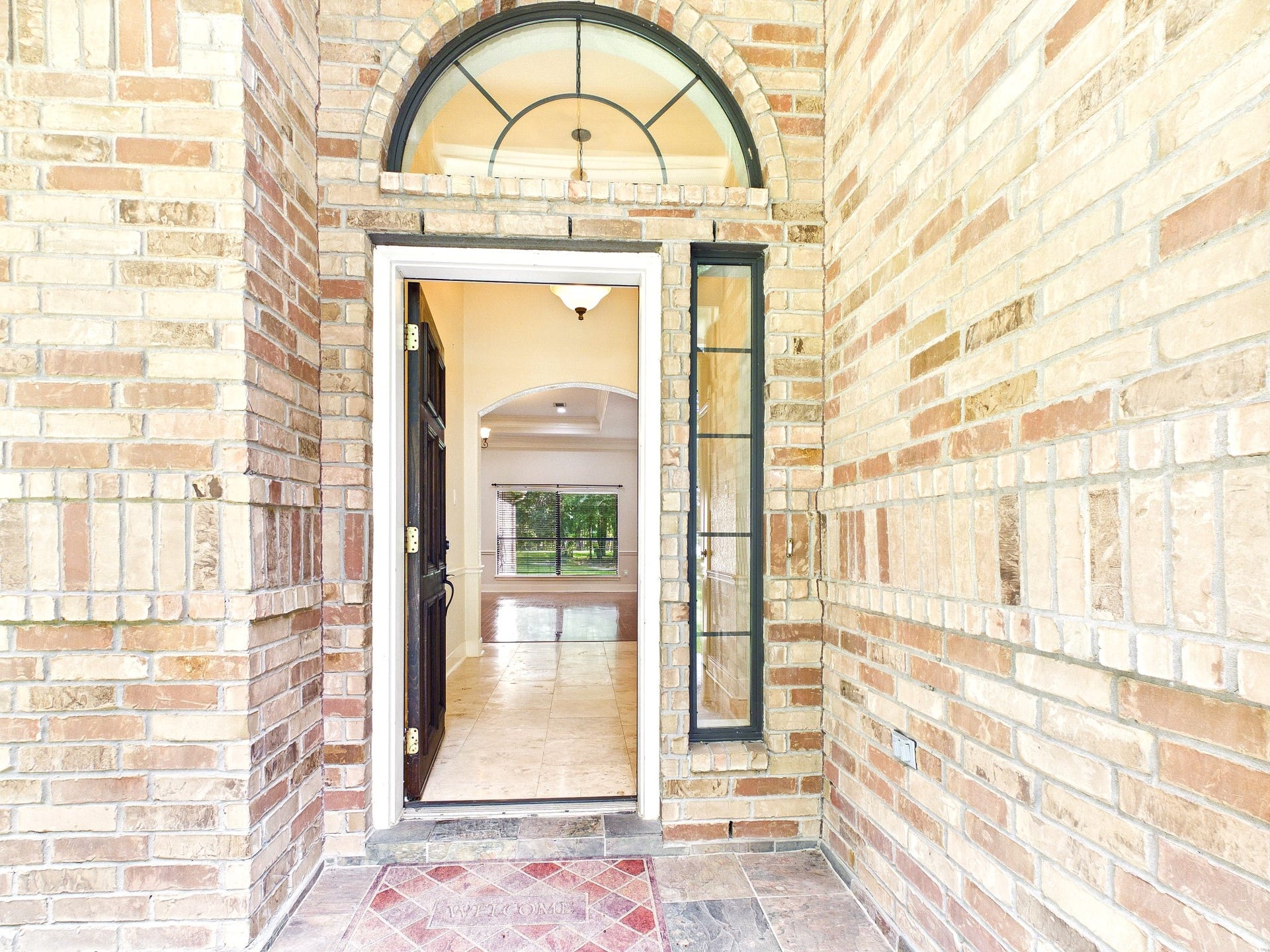 19521 Desna Drive, Porter, TX 77365 Welcome to your new home! This inviting entrance features a classic brick exterior with an arched window above the door, leading to a bright, spacious interior with tile flooring. Perfect for creating lasting first impressions.