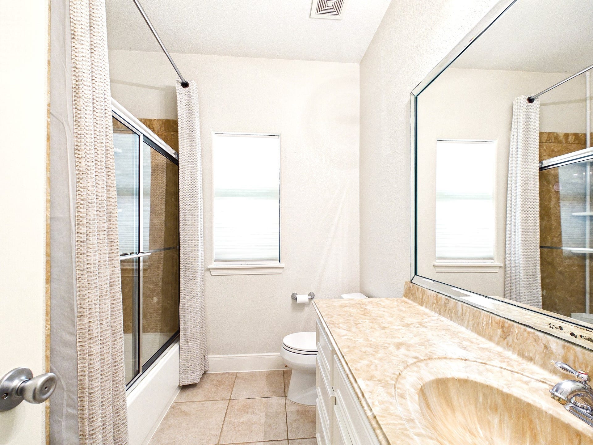 19521 Desna Drive, Porter, TX 77365 Bright and clean second bathroom featuring a large mirror, countertop space, tiled floor, and a shower-tub combo with sliding glass doors.