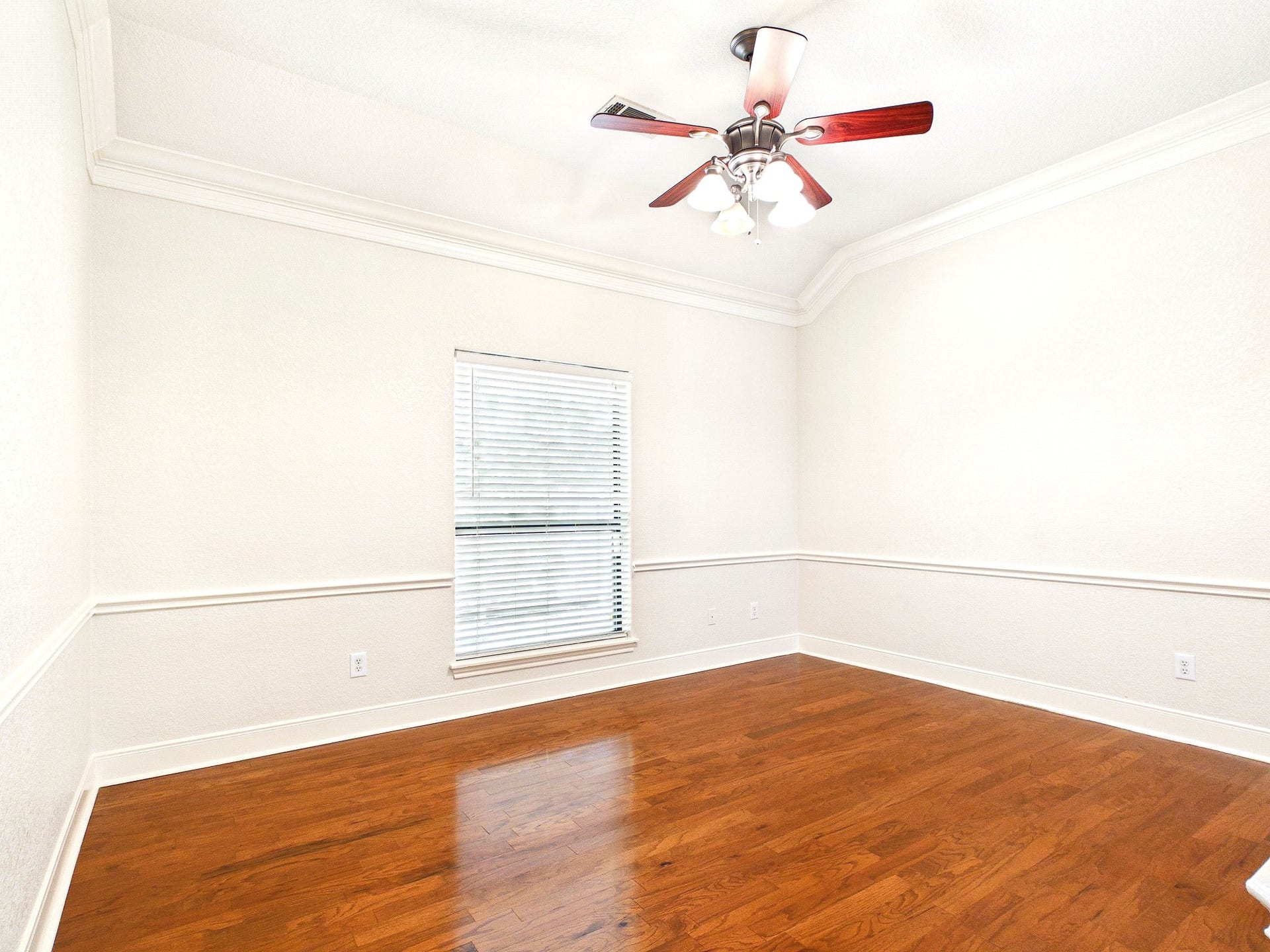 19521 Desna Drive, Porter, TX 77365 This bright, spacious room features hardwood floors, a ceiling fan with lights, and a large window with blinds, perfect for natural light. The neutral walls and crown molding add a touch of elegance.
