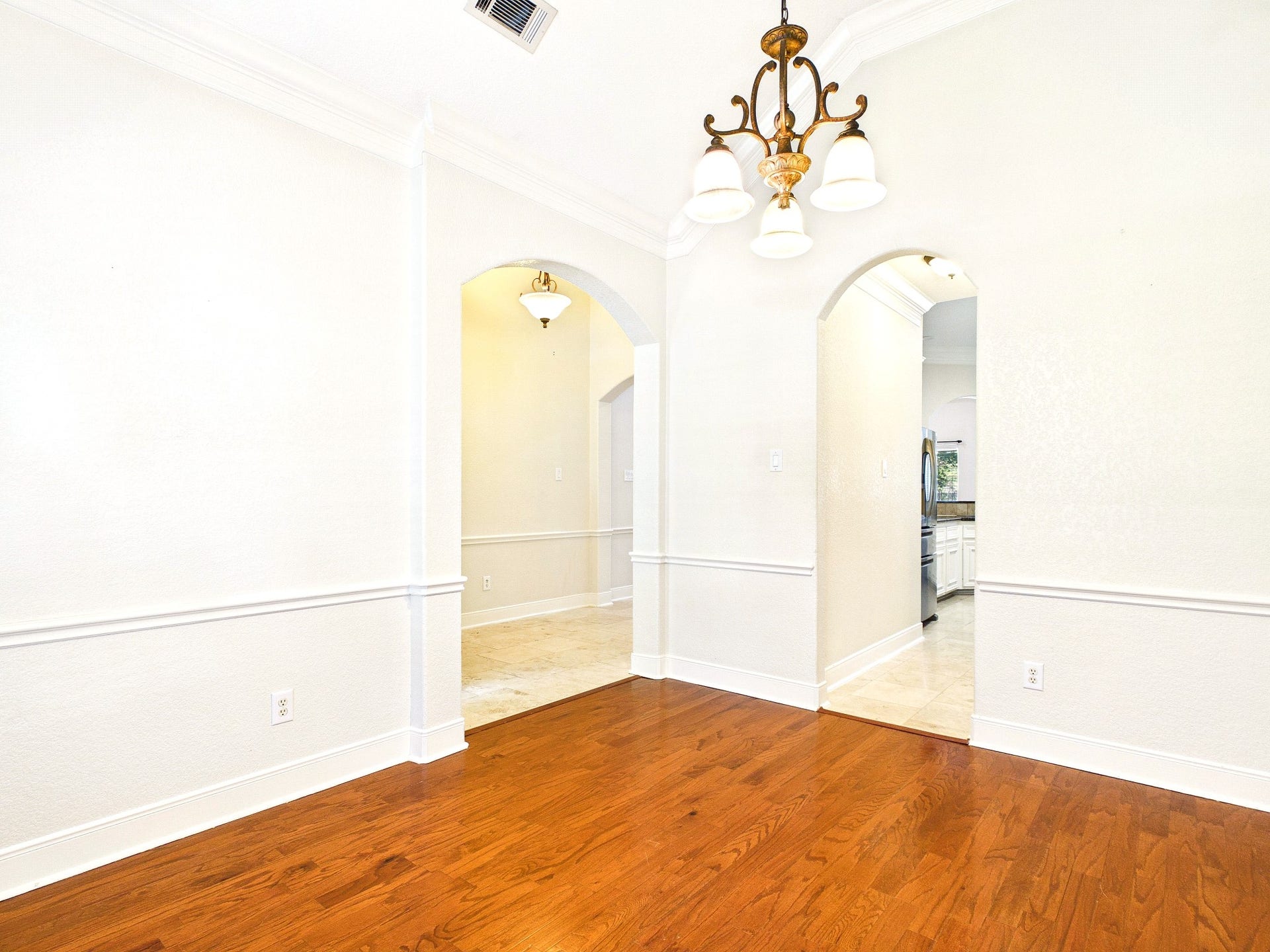 19521 Desna Drive, Porter, TX 77365 This photo showcases a bright, open dining room with polished hardwood floors, neutral walls, and elegant crown molding. Two arched doorways lead to adjacent areas, and a classic chandelier adds a touch of sophistication.