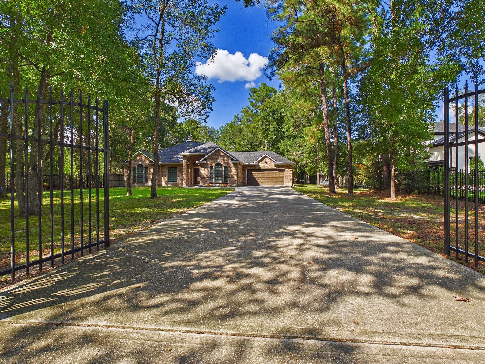 19521 Desna Drive, Porter, TX 77365 This photo showcases a charming brick home nestled among lush trees, featuring a long driveway leading up to a gated entrance, offering both privacy and scenic beauty.