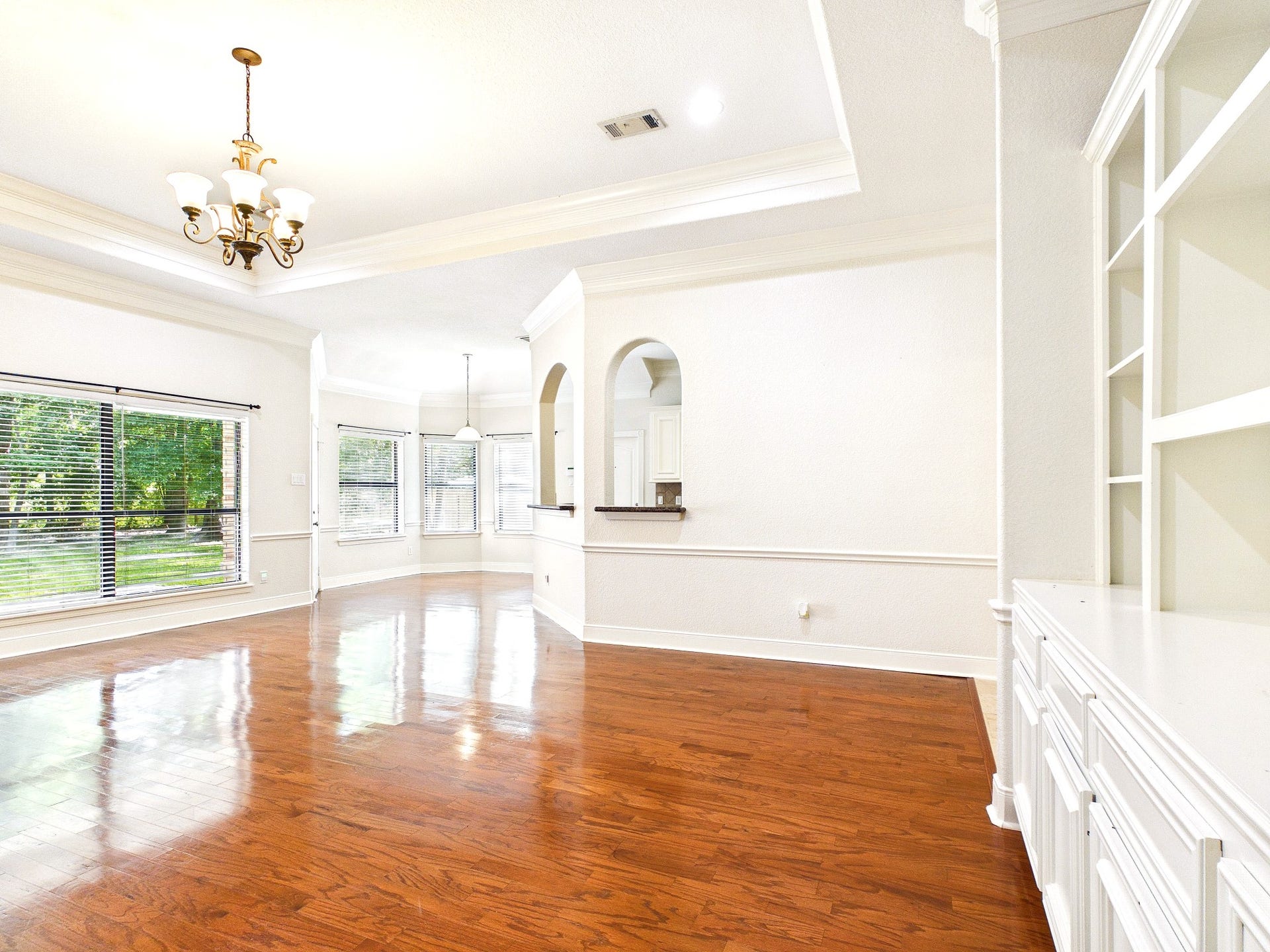 19521 Desna Drive, Porter, TX 77365 This spacious, light-filled living area features elegant hardwood floors, a stylish chandelier, built-in shelving, and large windows with views of the expansive backyard. The open layout connects to a cozy dining nook, ideal for entertaining.