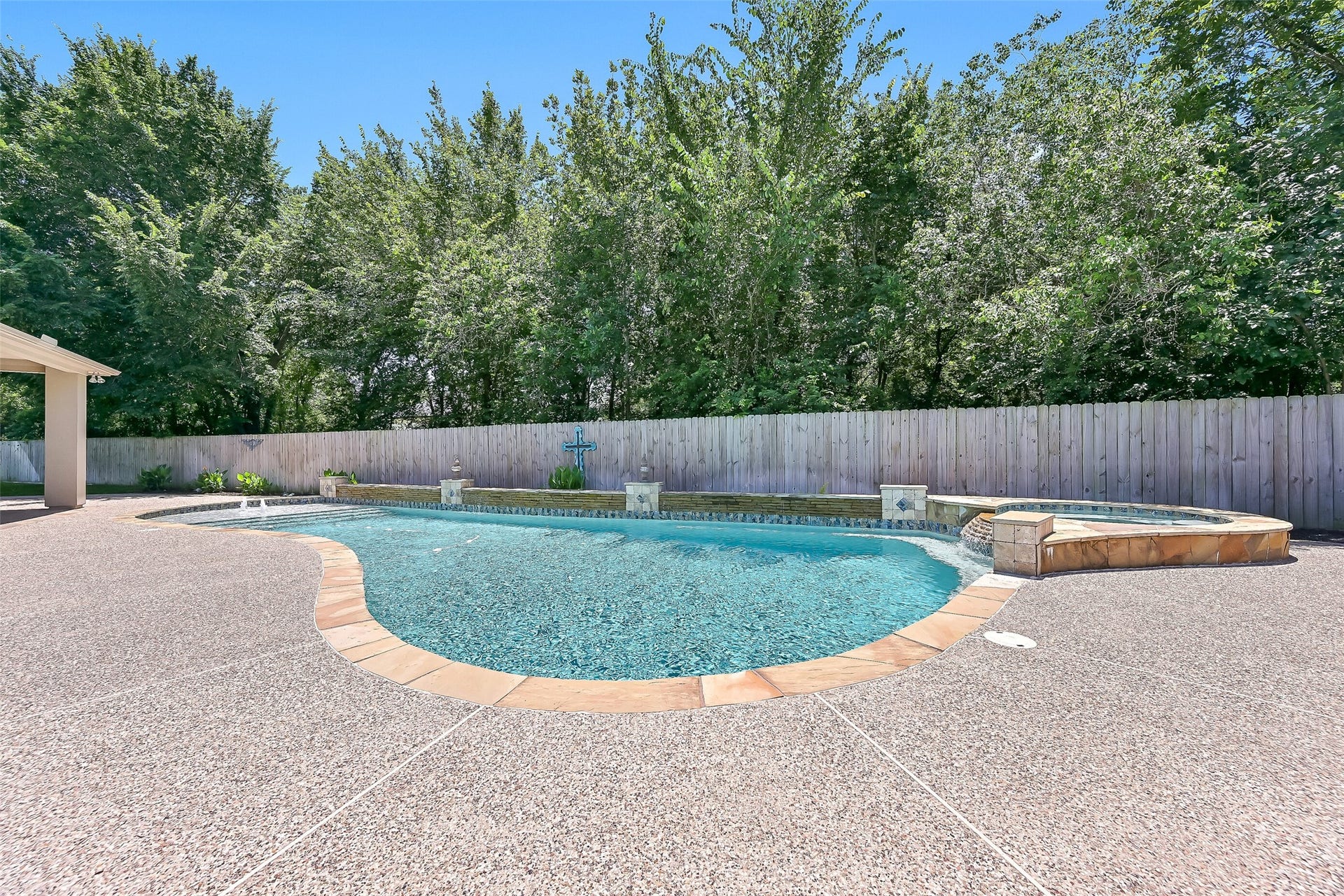 2304 Halls Creek Court, Friendswood, TX 77546 Another view highlights the expansive freeform pool, raised spa, textured decking, and serene wooded backdrop that adds exceptional privacy and shade to this pie-shaped backyard.