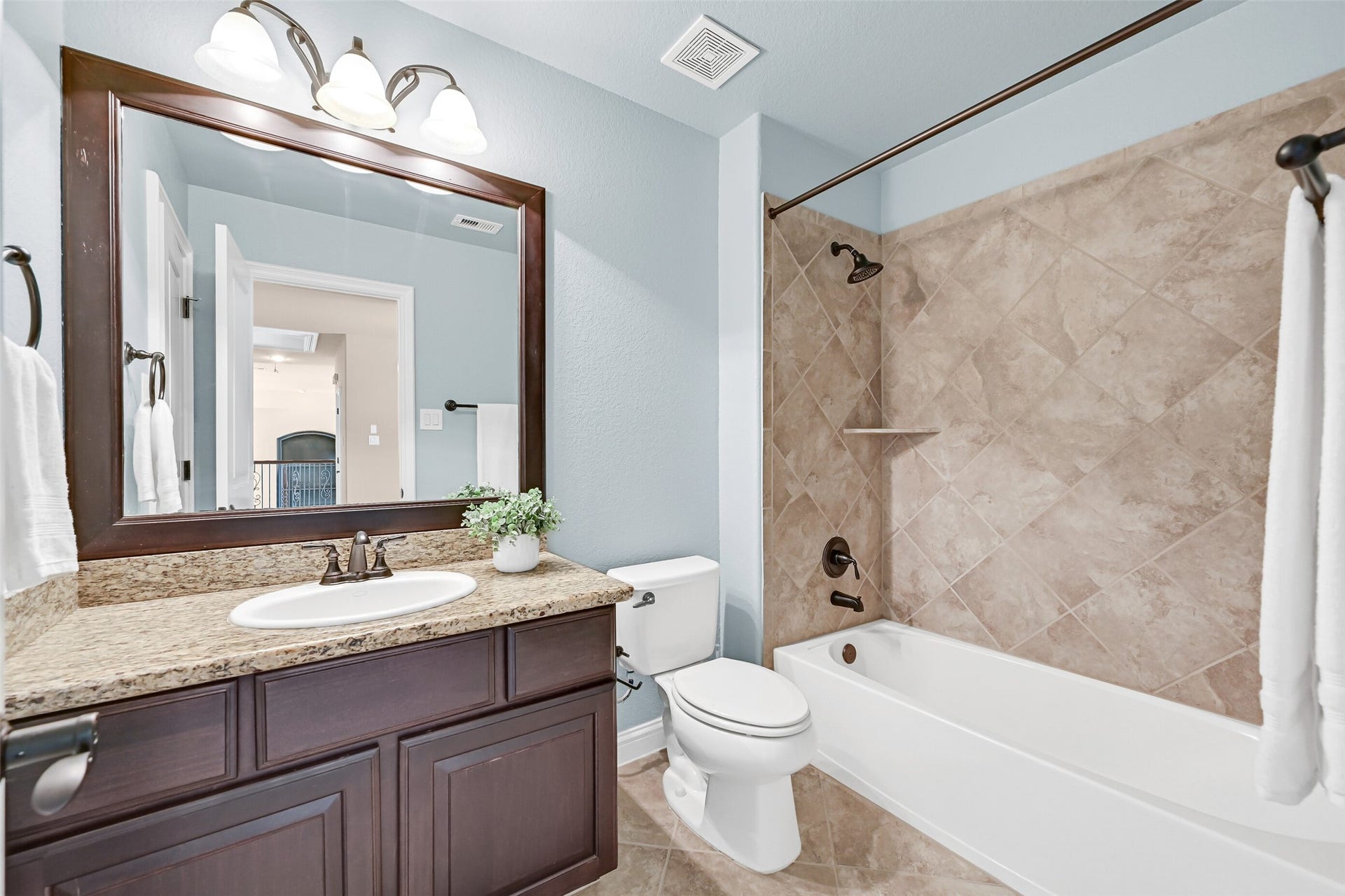 2304 Halls Creek Court, Friendswood, TX 77546 This private en suite bath features granite counters, a single basin sink, a framed mirror, tile flooring, and a beautifully tiled tub/shower surround with coordinating bronze fixtures.