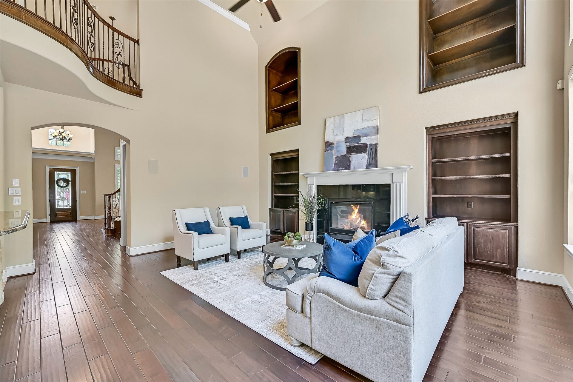 2304 Halls Creek Court, Friendswood, TX 77546 The family room makes an unforgettable first impression with 20-foot ceilings, rich engineered wood floors, dramatic floor-to-ceiling windows, and custom built-in shelving stretching toward the second story. A grand gas fireplace with granite tile surround and a milled wood mantle anchors the space while backyard views pour in from every angle.