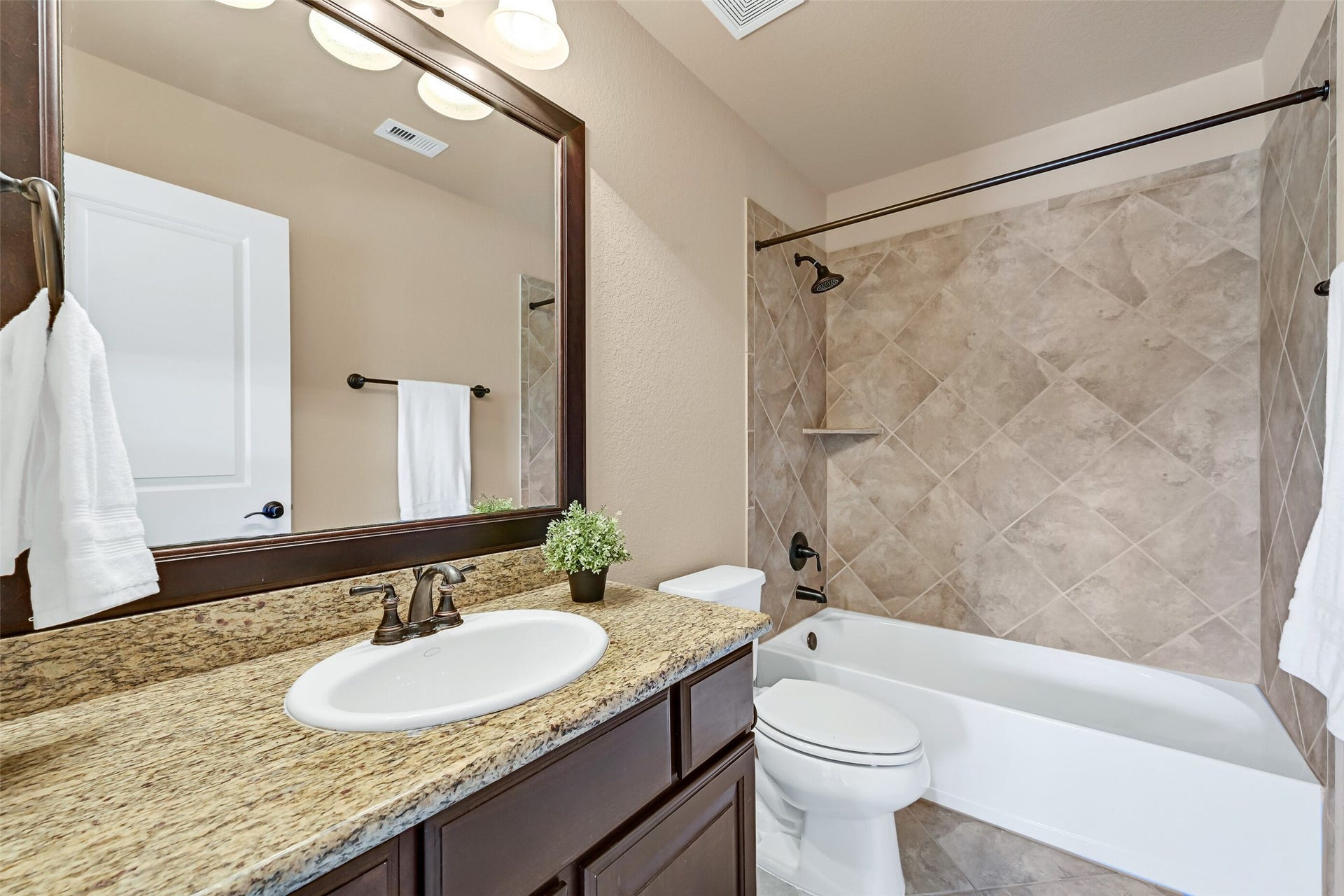 2304 Halls Creek Court, Friendswood, TX 77546 This en suite bathroom continues the homes consistent high-end finishes with granite counters, a single basin sink with oil rubbed bronze faucet, dark espresso stained cabinetry, tile flooring, and a tiled tub/shower combination.