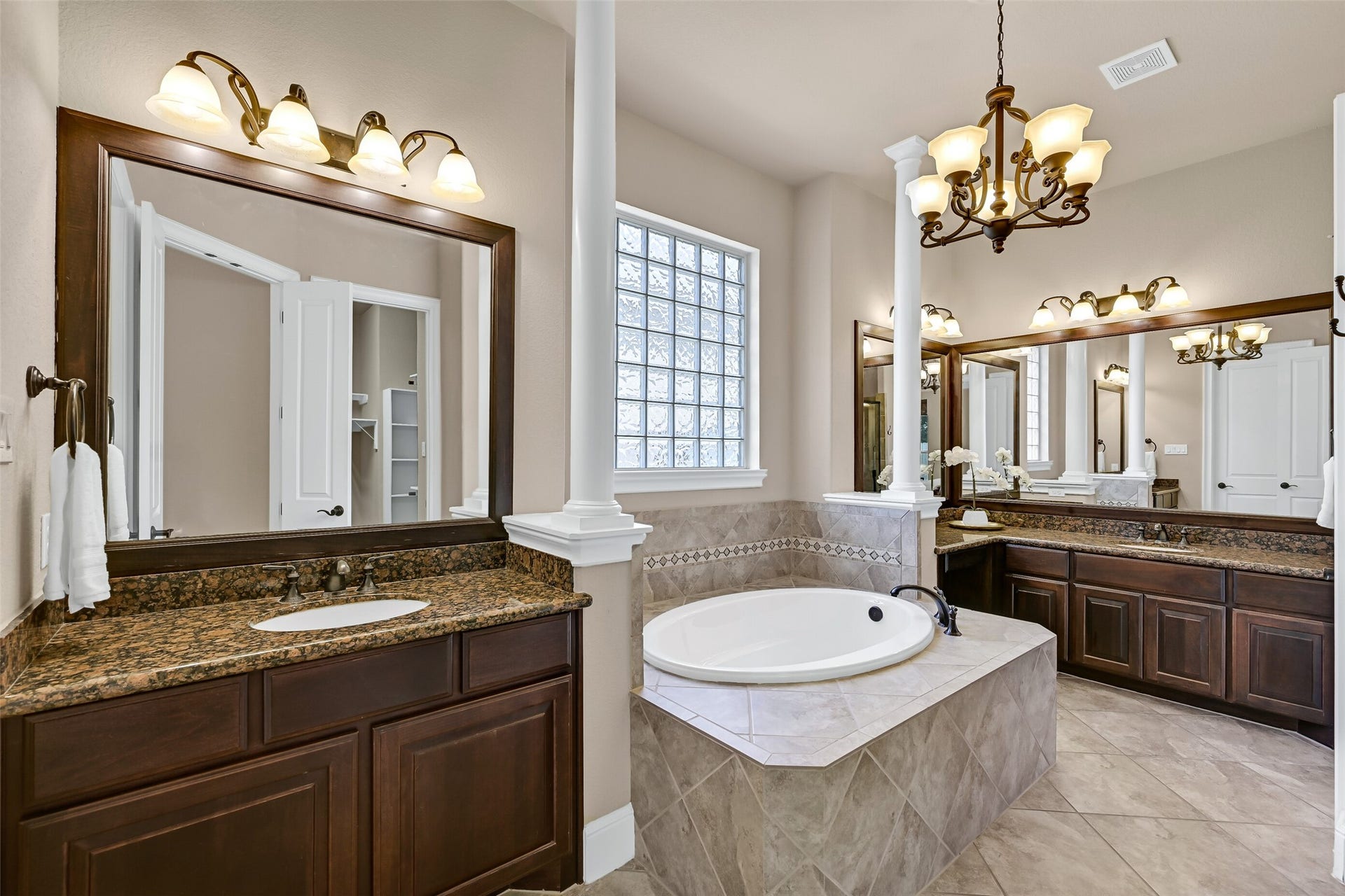 2304 Halls Creek Court, Friendswood, TX 77546 The spa-inspired primary bathroom features separate granite-topped vanities with rich espresso cabinetry, a soaking tub framed by decorative tilework and glass block windows, elegant lighting, and soaring ceilings that make the entire space feel open and luxurious.