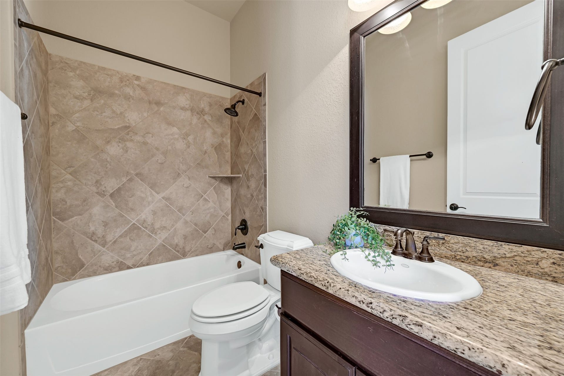 2304 Halls Creek Court, Friendswood, TX 77546 The en suite guest bath is finished with granite countertops, a single basin sink, rich wood cabinetry, oil-rubbed bronze fixtures, a framed mirror, and a tiled tub/shower surround that gives the space a clean, upscale feel.
