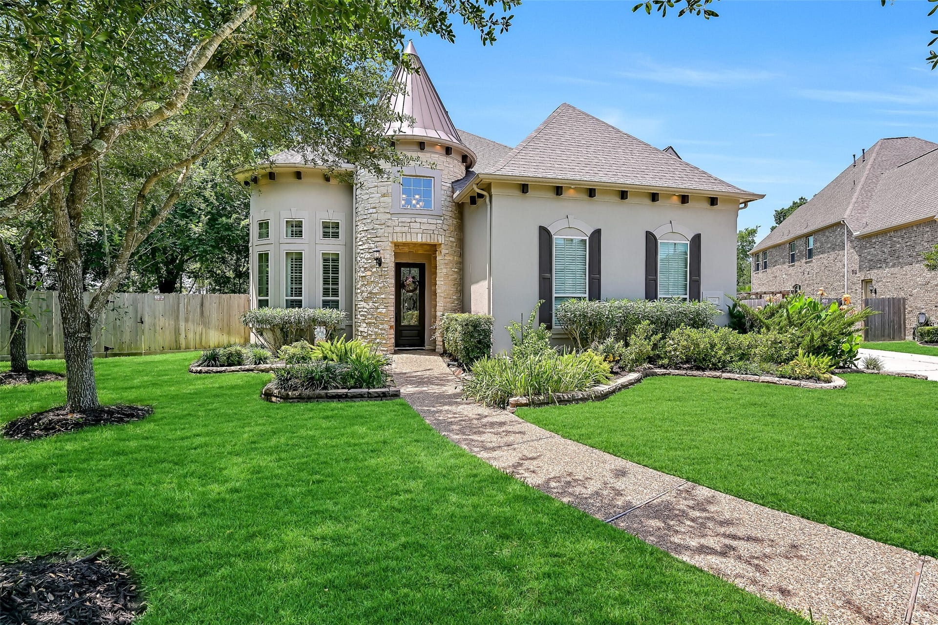 2304 Halls Creek Court, Friendswood, TX 77546 A curved walkway winds through lush landscaping to the impressive leaded glass front door, framed by stacked stone detailing and soaring turret architecture. Even before stepping inside, the combination of manicured greenery, custom exterior finishes, and stately design hints at the grand spaces waiting beyond the entry.