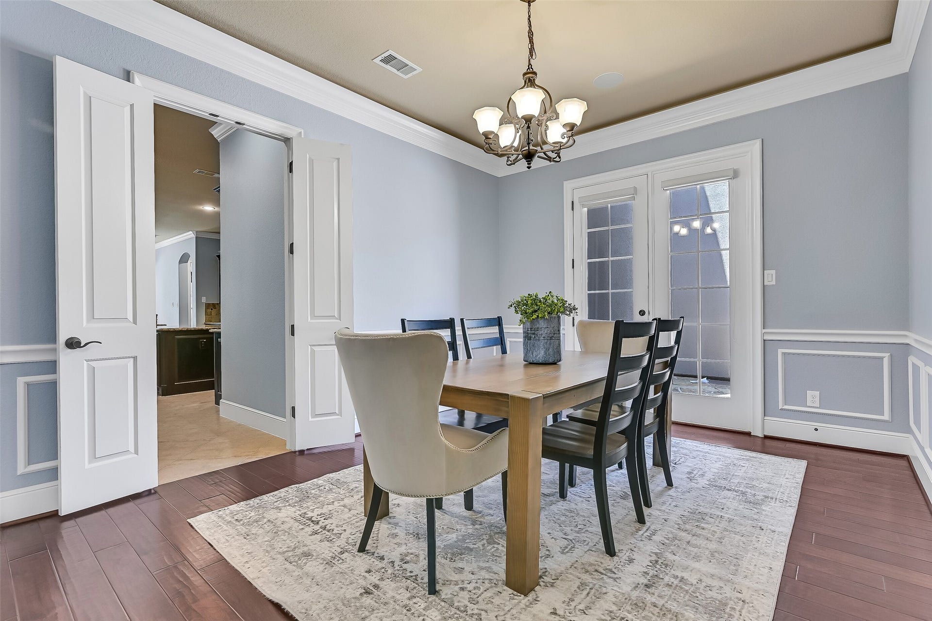 2304 Halls Creek Court, Friendswood, TX 77546 Another view of the formal dining room showcases the detailed millwork, rich wood flooring, and direct access to the butlers pantry and kitchen beyond, while the courtyard-facing French doors allow natural light to pour into the space throughout the day.