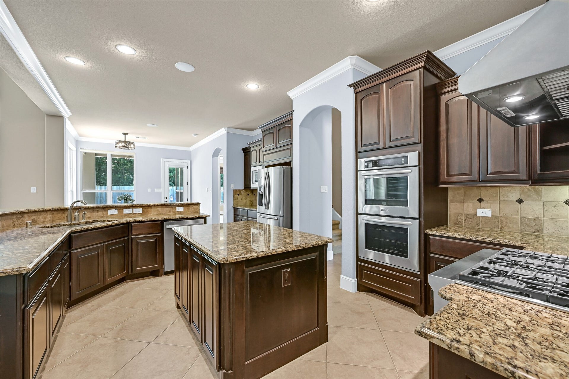 2304 Halls Creek Court, Friendswood, TX 77546 Another angle of the kitchen showcases the oversized island, extensive granite workspace, stainless appliances, and thoughtful layout that keeps everything within easy reach while still maintaining an open, airy feel. Through the arched entrance on right, you can catch a glimpse of the rear staircase of the home.