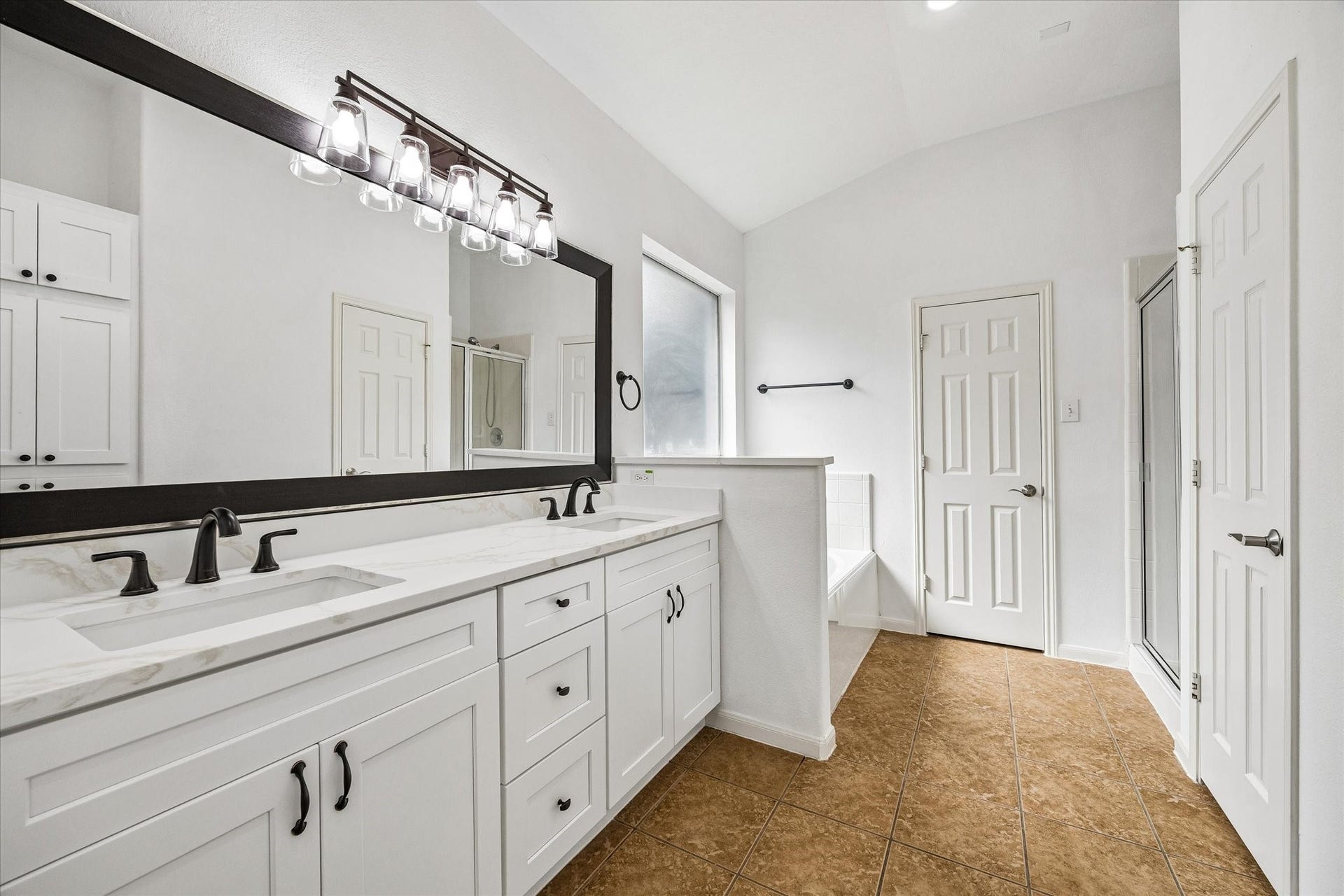6741 Hidden Colony Lane, Dickinson, TX 77539 Spacious bathroom with a double vanity, sleek black fixtures, and a large mirror. Natural light flows in through the window, illuminating the elegant tile flooring and providing a bright, airy atmosphere.