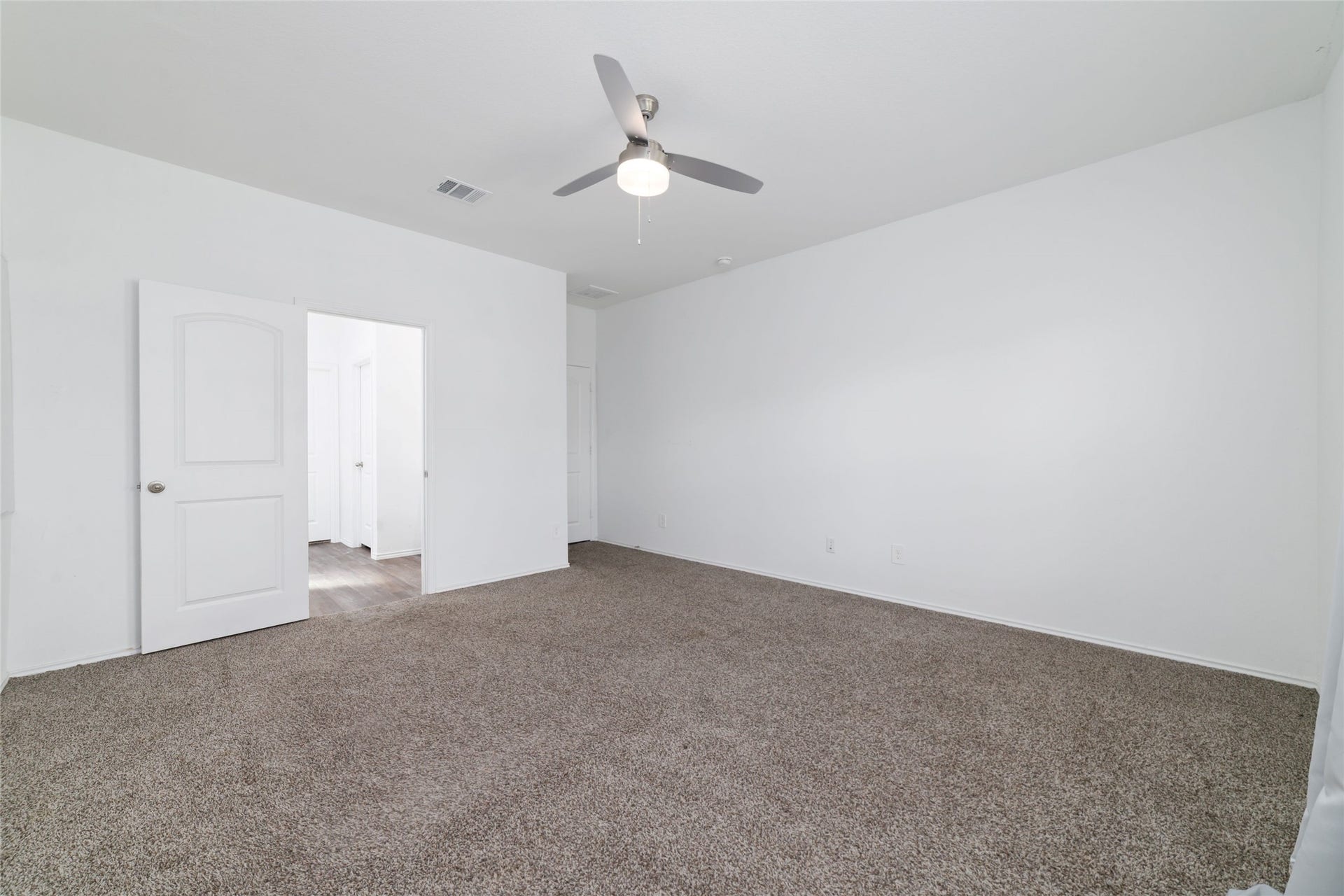 Offering generous proportions and exceptional privacy on the ground floor, the owner's bedroom features soft neutral carpeting, a modern brushed-nickel ceiling fan, and vast wall space ideal for a large king-size furniture suite. An elegant doorway provides direct, seamless access into the luxurious en-suite bathroom and expansive walk-in closet