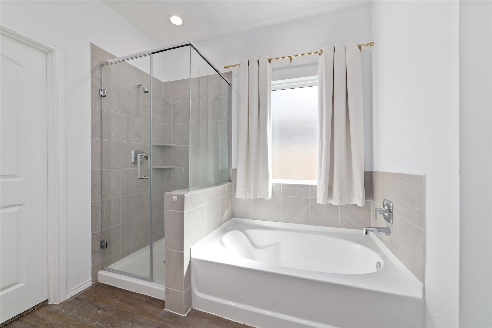 Interior view of a modern full bathroom featuring dark wood-look flooring, a white vanity with an undermount sink, a large mirror, and a tiled shower/bathtub combination with standard fixtures