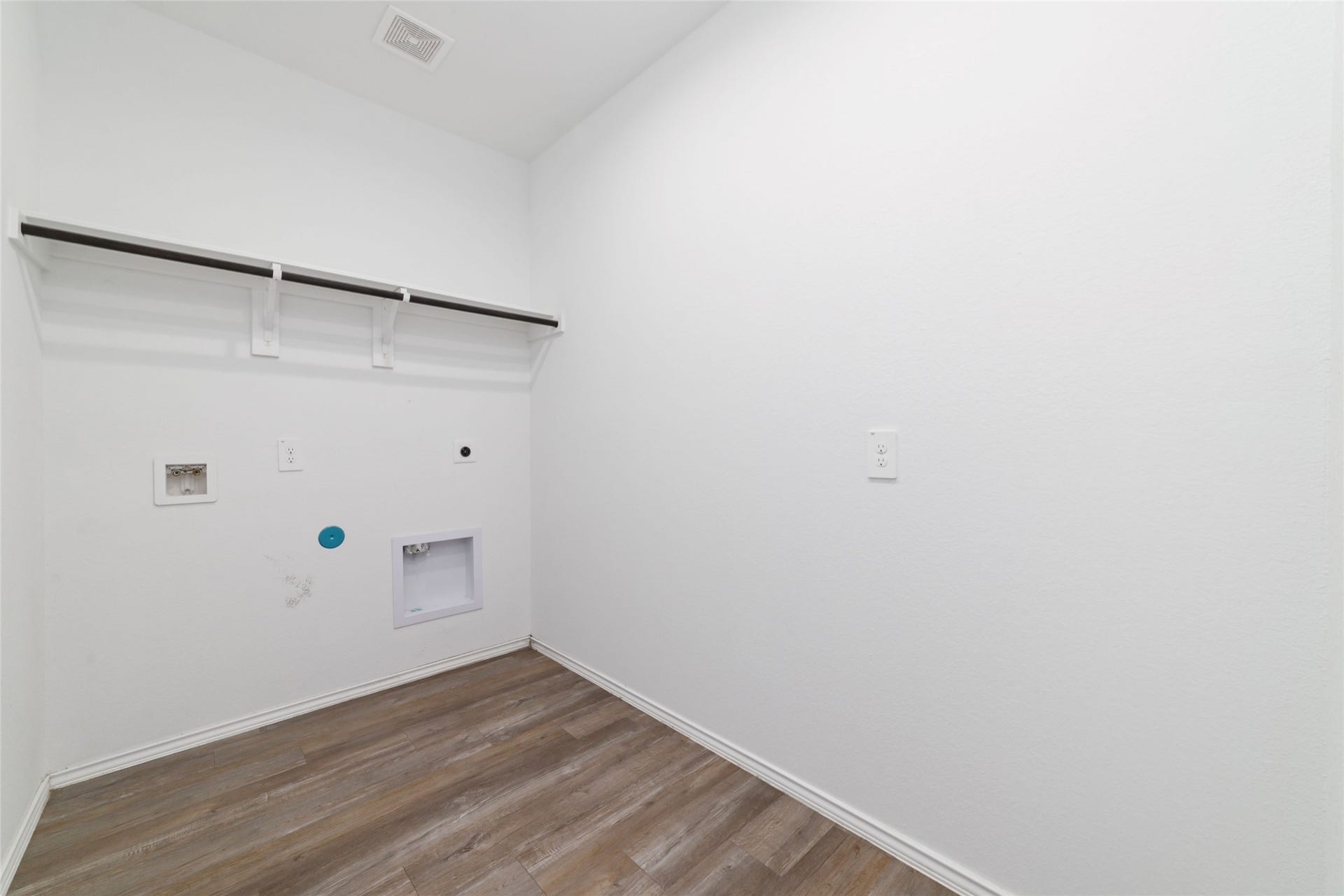 Spacious, dedicated laundry room featuring dark wood-look flooring and a built-in overhead shelf with a hanging rod for convenient storage and organization. To complete this truly turnkey package, the seller is including the washer and dryer with the salesaving buyers thousands in out-of-pocket expenses on move-in day!