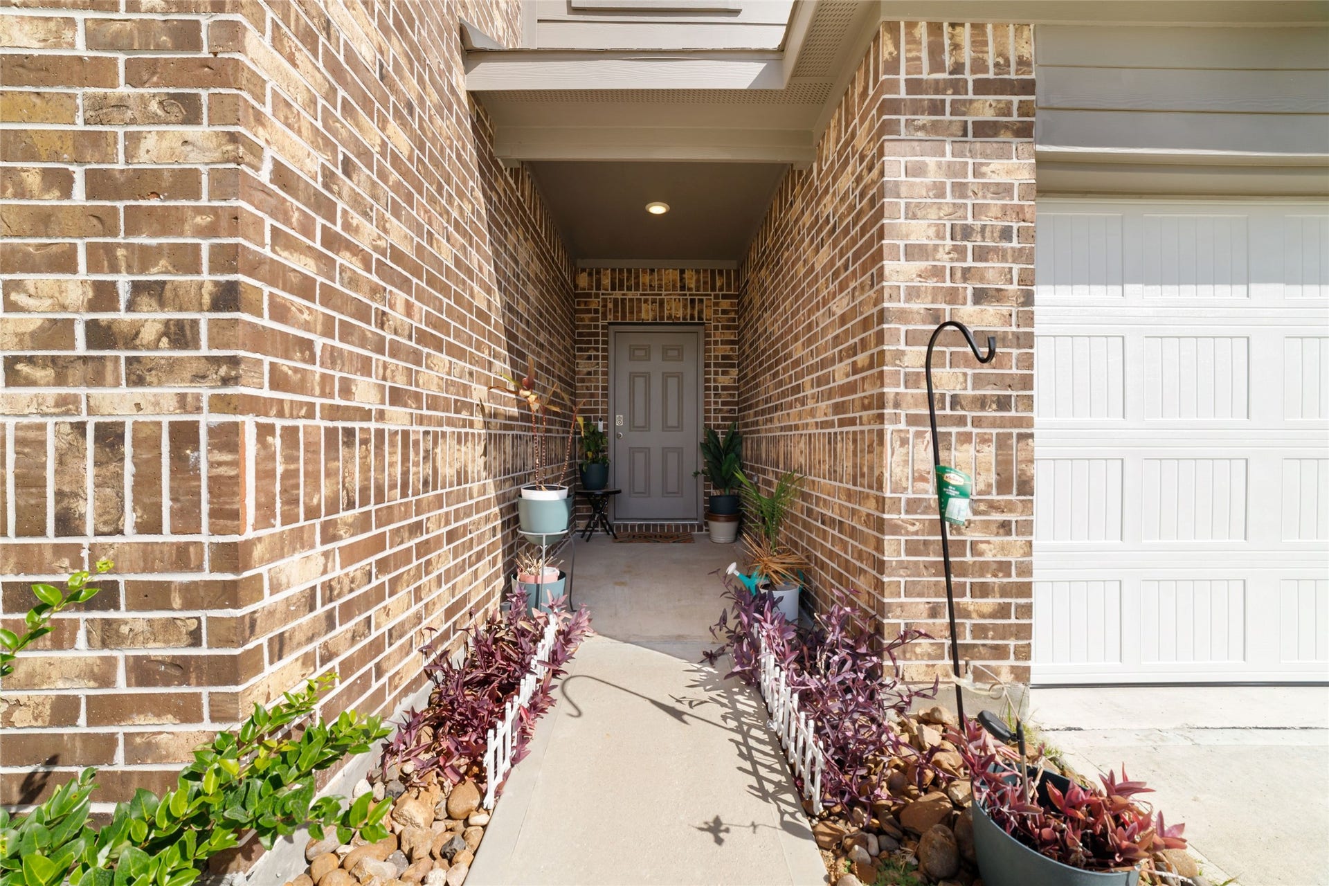 Focused close-up of the front entryway and porch alcove, featuring a modern grey front door set within brick walls with small potted plants, a welcome mat, and decorative accents