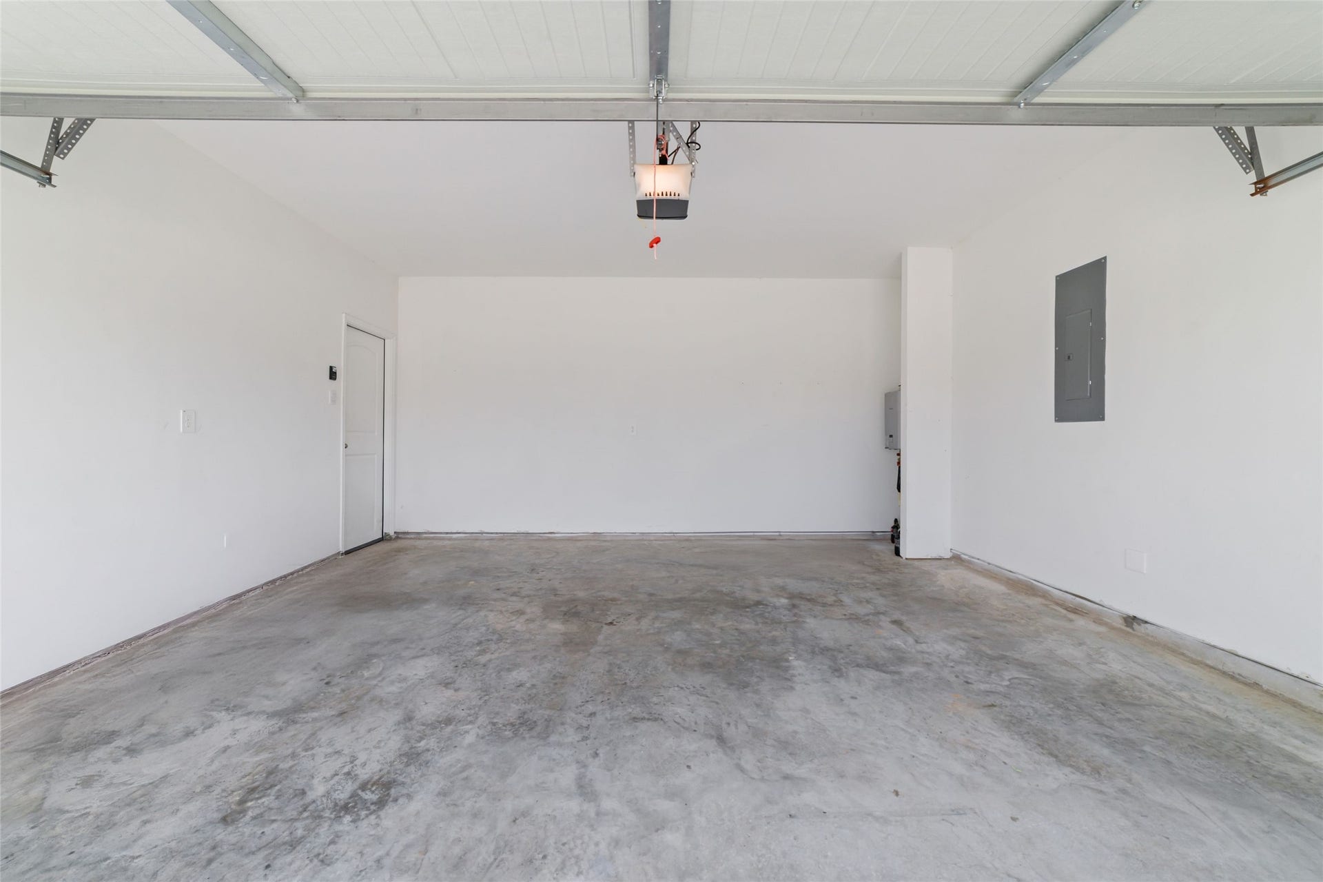 Inside view of a clean, empty attached two-car garage with white walls, a durable concrete floor, and an overhead automated door opener mechanism
