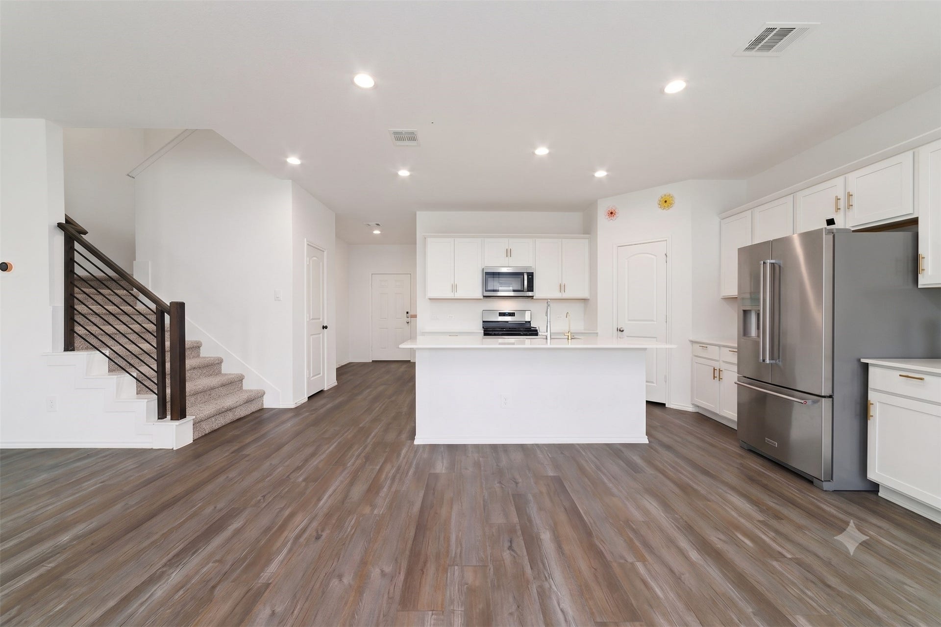 A complementary wide view of the modern open-plan kitchen and living space, showing the full appliance suite, central island, and the main staircase under recessed lighting.