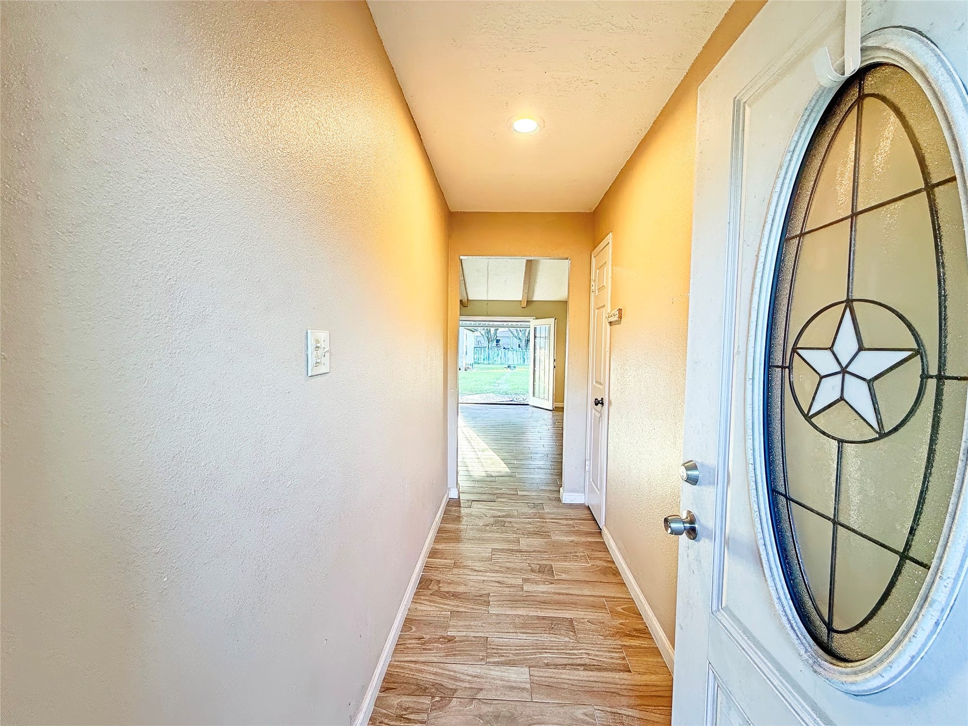 8116 Gulick Lane, Houston, TX 77075 Inviting entryway with wood-style flooring leads to a bright living space and a view of the backyard, highlighted by a distinctive star-patterned glass door.