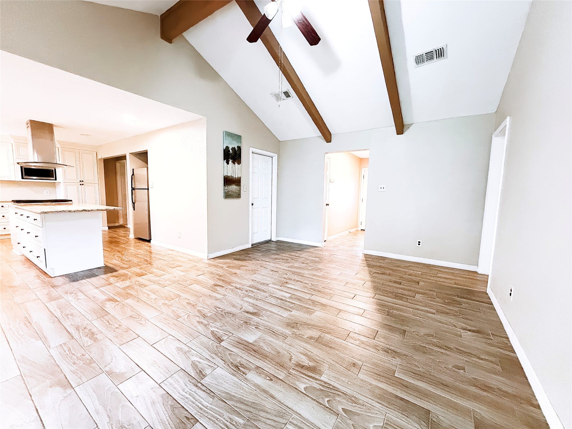 8116 Gulick Lane, Houston, TX 77075 Spacious open-concept living area with vaulted ceilings, exposed wooden beams, and elegant wood-look tile flooring leading into a bright, modern kitchen.