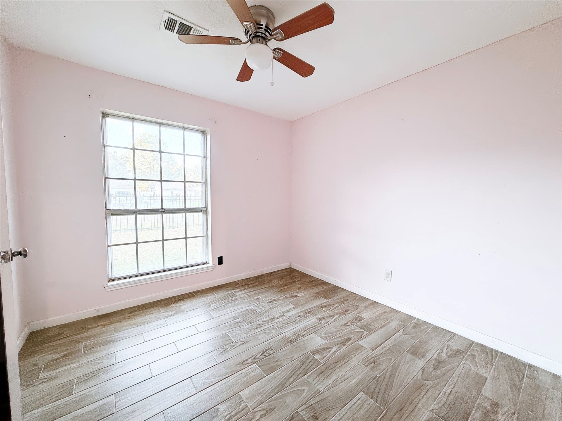 8116 Gulick Lane, Houston, TX 77075 Charming bedroom with soft pink walls, wood-look tile flooring, and abundant natural light from a large window, complemented by a ceiling fan.