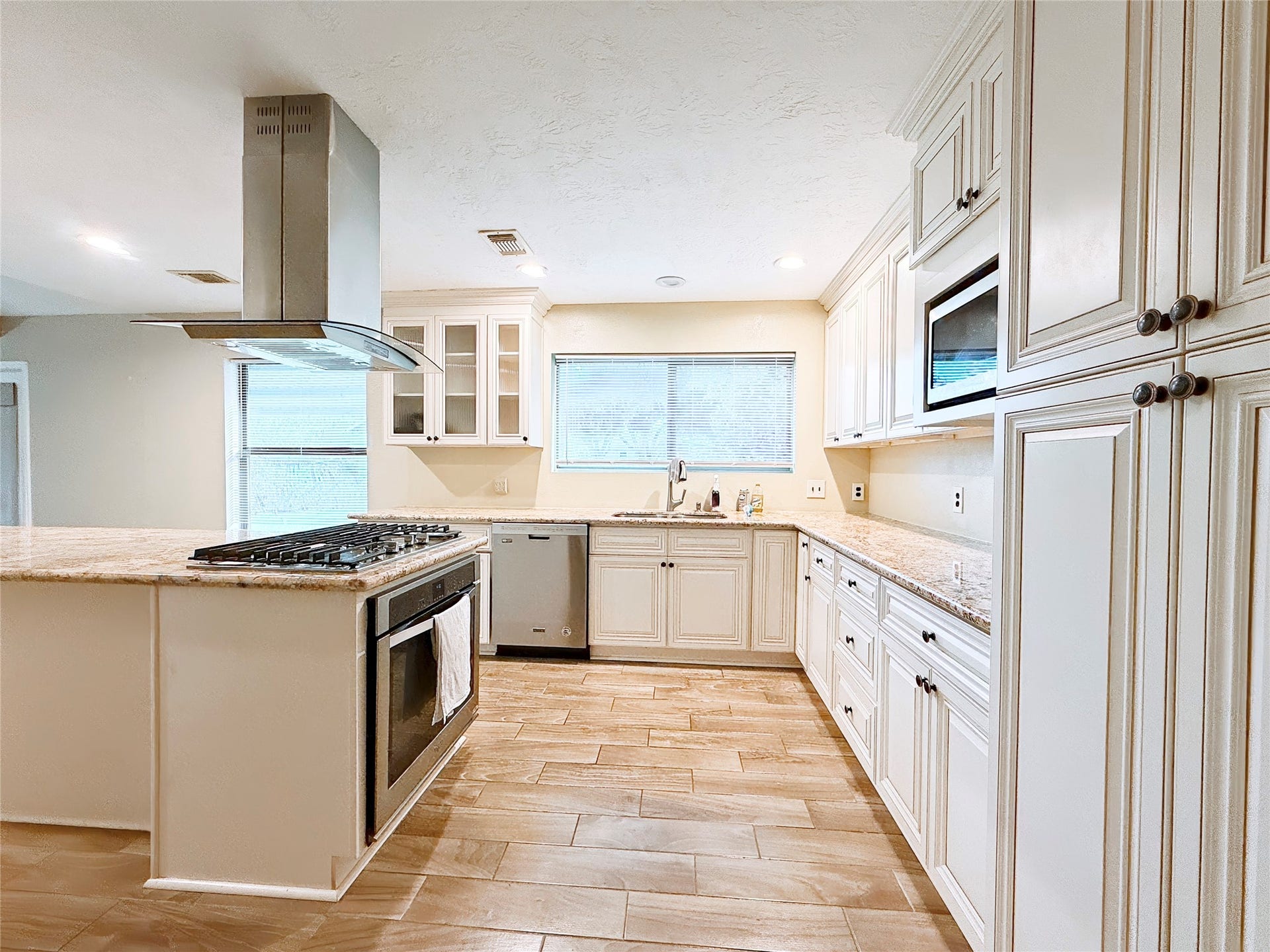 8116 Gulick Lane, Houston, TX 77075 Spacious kitchen featuring elegant white cabinetry, granite countertops, and a modern stainless steel stove with a sleek range hood, complemented by ample natural light and tiled flooring.