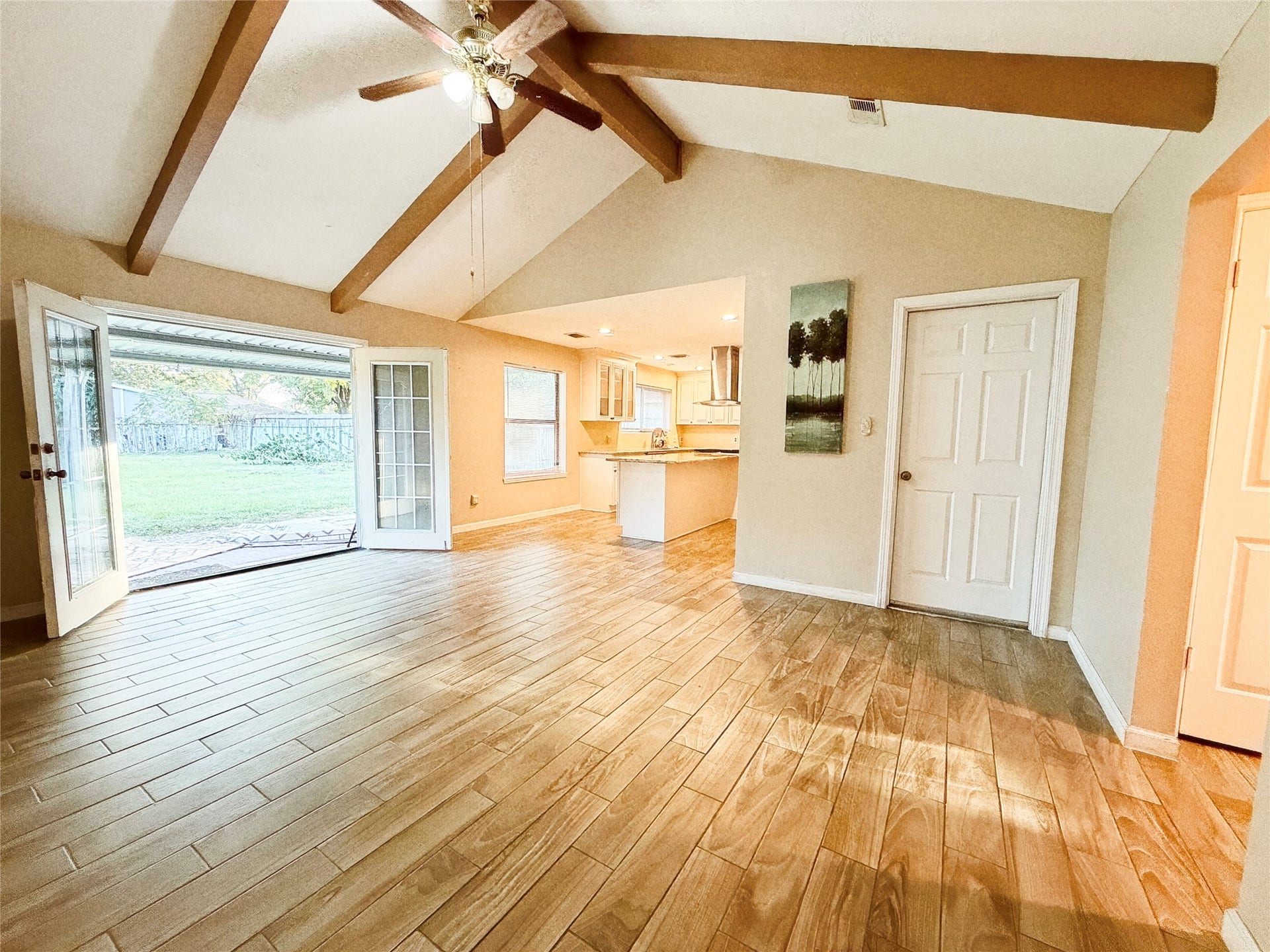 8116 Gulick Lane, Houston, TX 77075 Spacious living area with vaulted ceilings and exposed beams, featuring elegant wood-look tile flooring and French doors leading to a serene backyard.