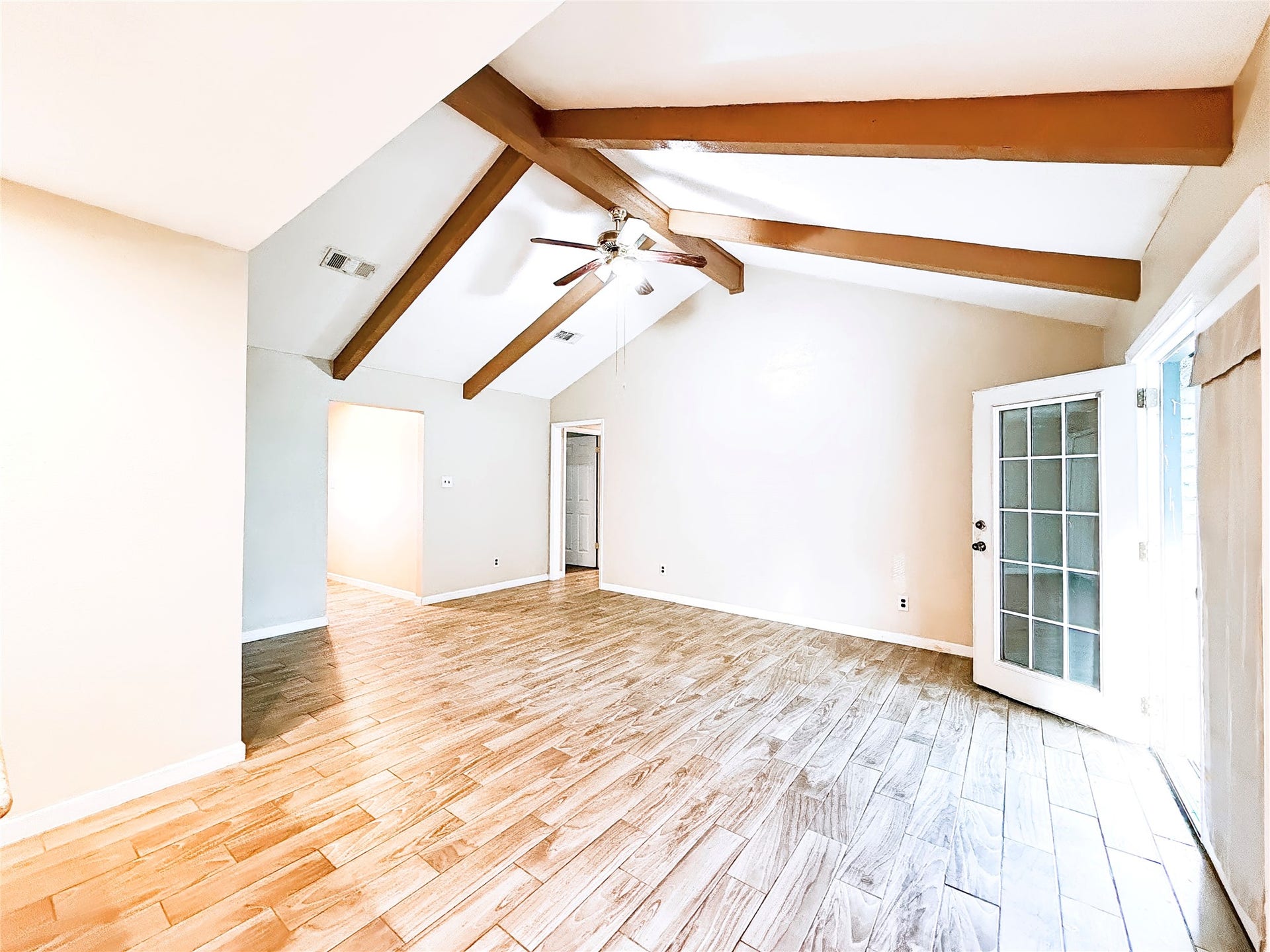 8116 Gulick Lane, Houston, TX 77075 Spacious living area with high vaulted ceilings and exposed wooden beams, featuring elegant wood-look tile flooring and abundant natural light from French doors.