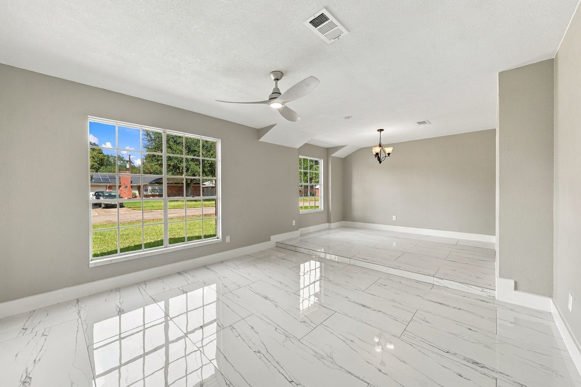 1023 Twinbrooke Drive, Houston, TX 77088 The empty living room shows bright tile flooring, wide windows, and generous open wall space. Virtually staged.