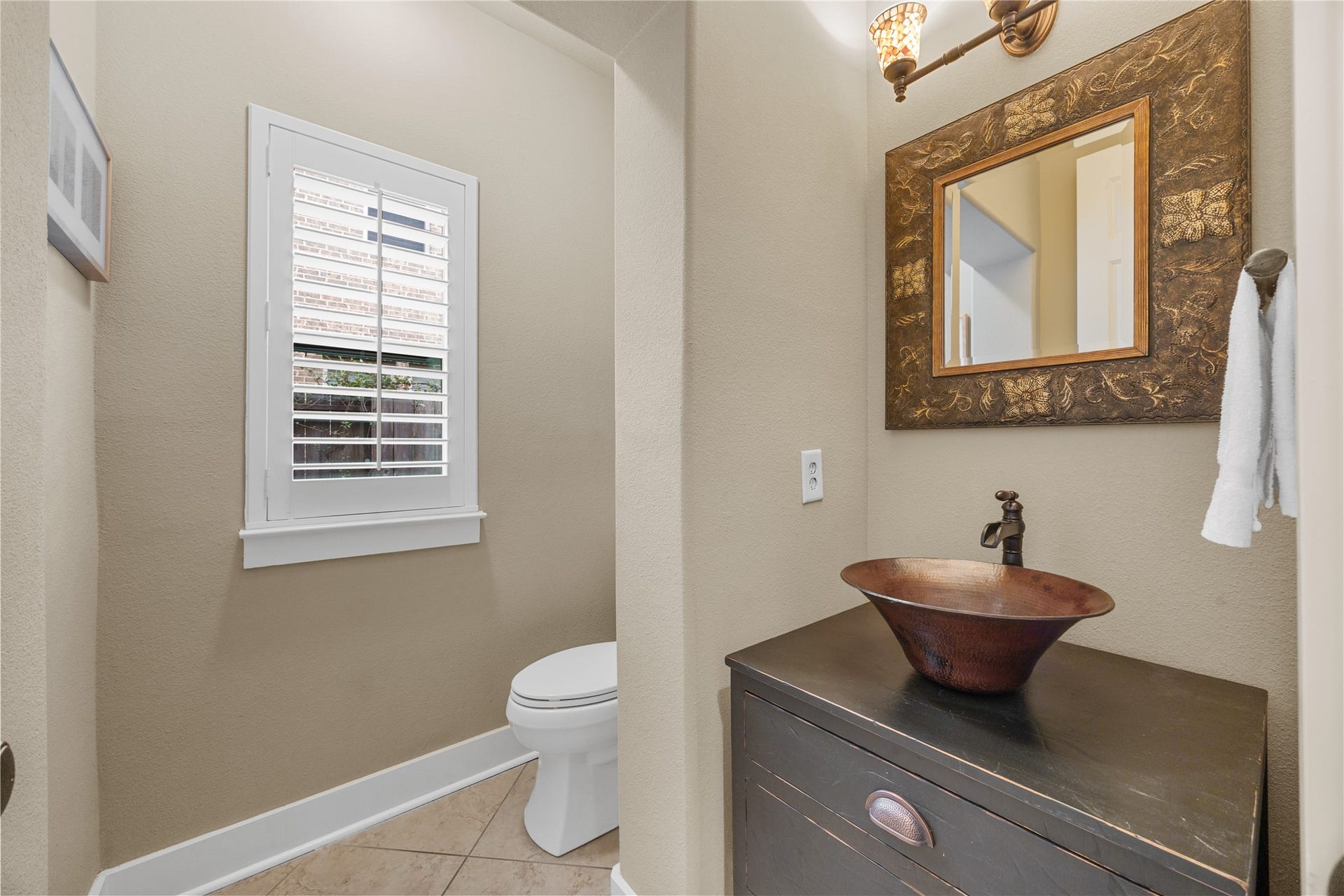18515 Duke Lake Drive, Spring, TX 77388 Charming powder room featuring a distinctive copper-toned vessel sink, decorative mirror, and plantation shutters.
