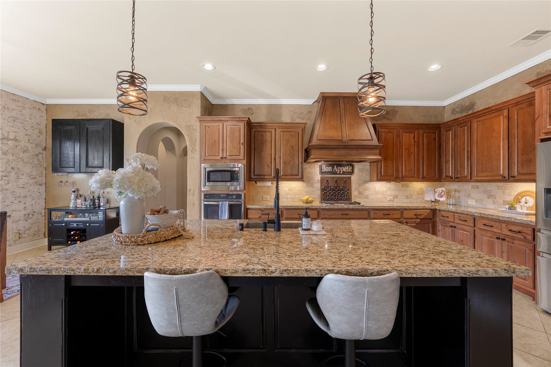 18515 Duke Lake Drive, Spring, TX 77388 The kitchen's oversized granite island offers generous prep space and seating, complemented by rich wood cabinetry, pendant lighting, stainless steel appliances, and a custom vent hood.