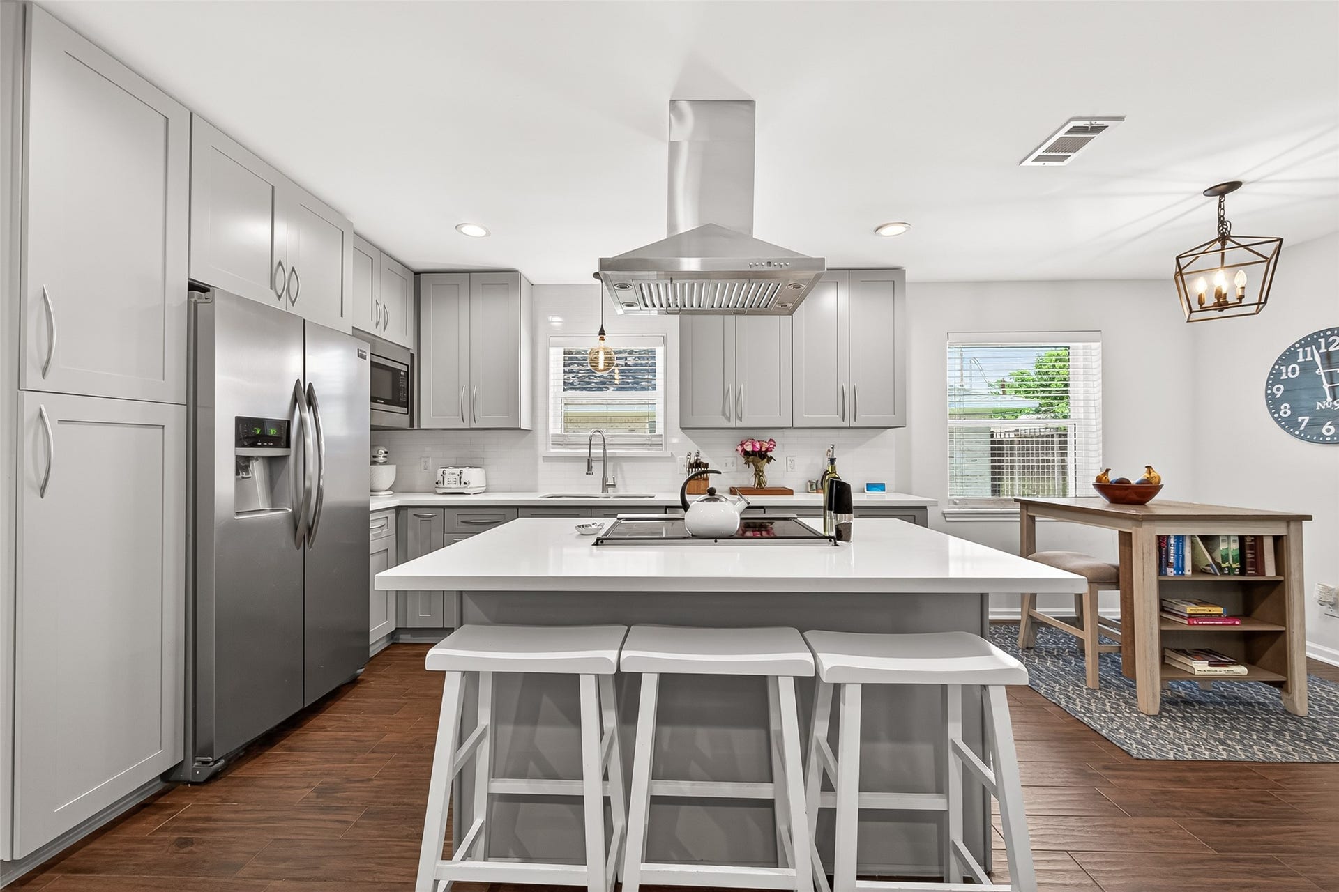 2610 Teague Road, Houston, TX 77080 This modern kitchen features sleek gray cabinets, stainless steel appliances, and a central island with bar seating. It has ample natural light, wood-like tile flooring, and a cozy dining nook, creating a stylish and functional space.