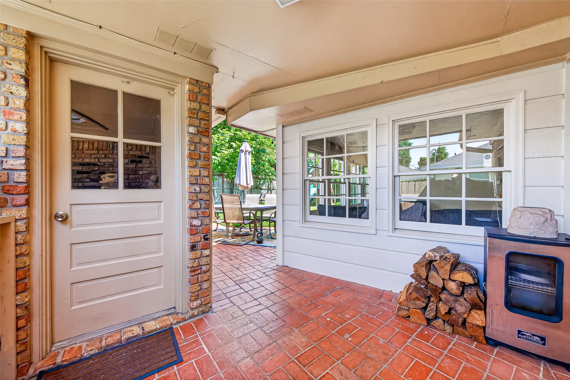 2610 Teague Road, Houston, TX 77080 This photo showcases a cozy patio area with brick flooring, a side door, and large windows providing natural light.