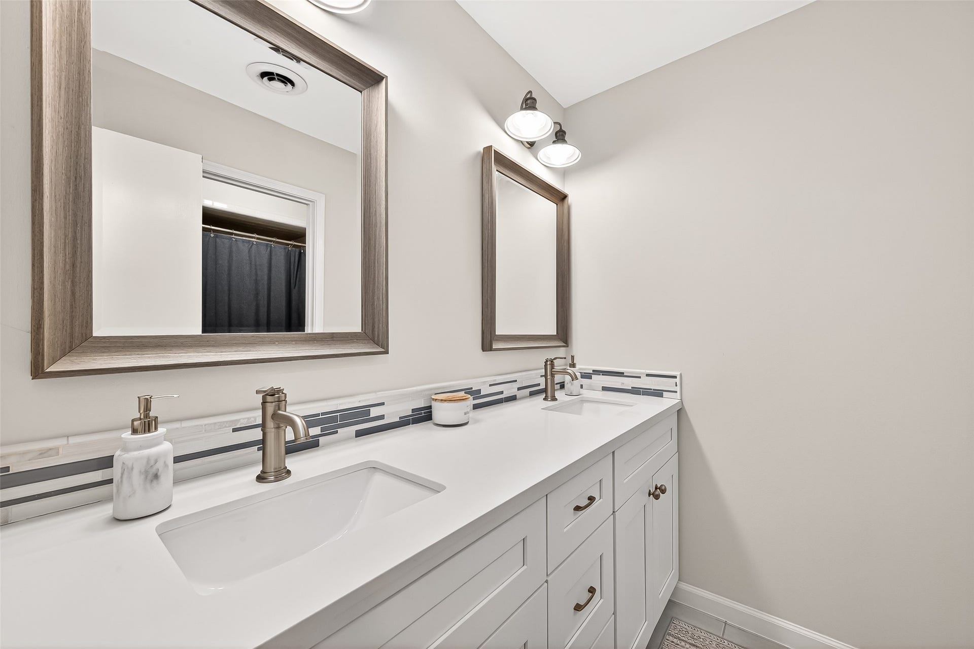2610 Teague Road, Houston, TX 77080 This modern bathroom features dual sinks with sleek fixtures, stylish framed mirrors, and a contemporary backsplash, offering both functionality and elegance.