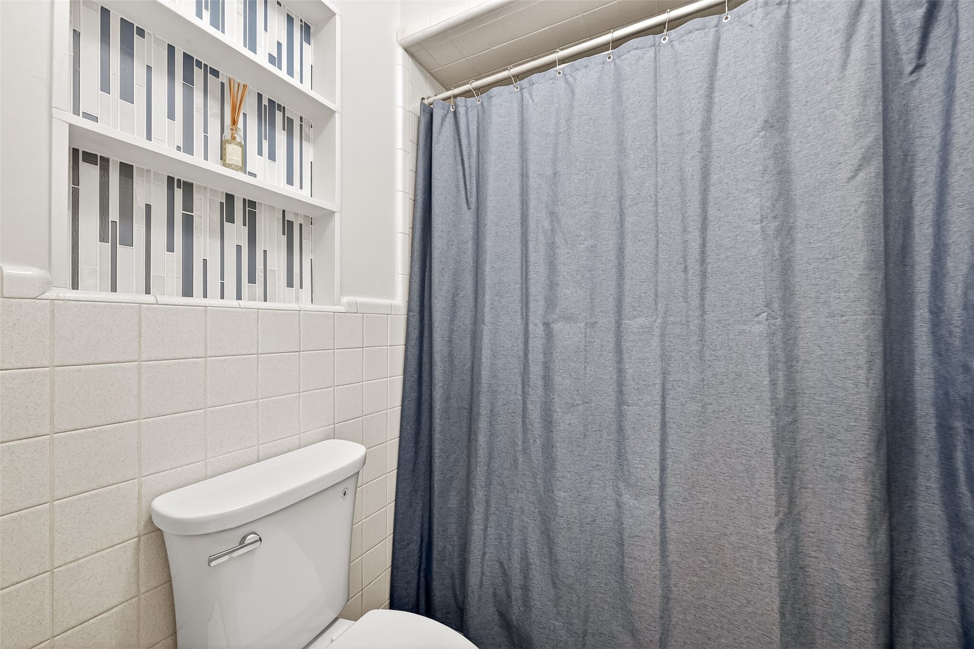 2610 Teague Road, Houston, TX 77080 This bathroom features a neatly tiled wall and a shower-tub combination. Built-in shelving provides stylish storage, accented with geometric tile patterns.