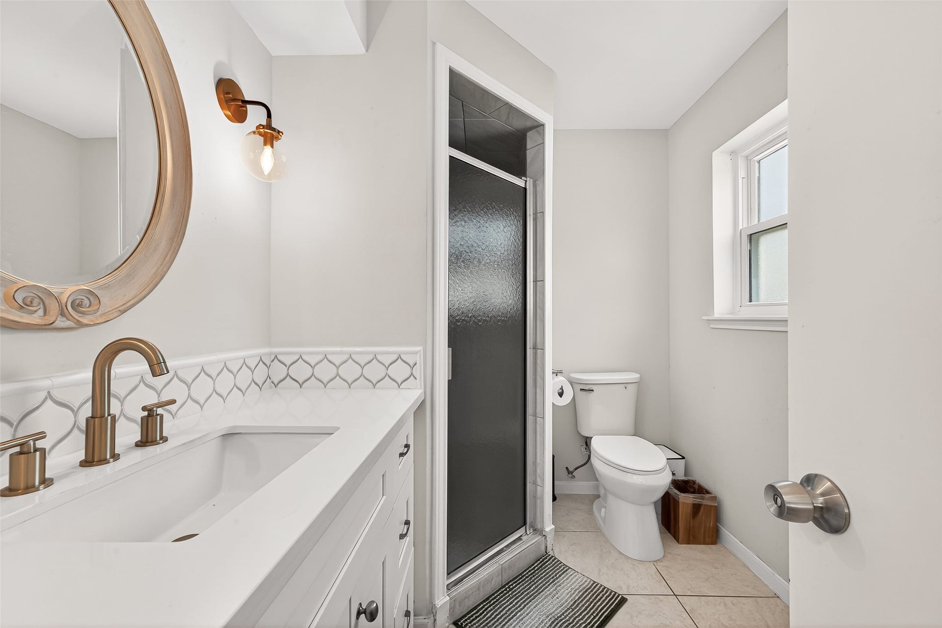 2610 Teague Road, Houston, TX 77080 This primary bathroom features a modern design with a large mirrored vanity, elegant fixtures, and a sleek glass shower. Natural light illuminates the space through a window, creating a bright and welcoming atmosphere.