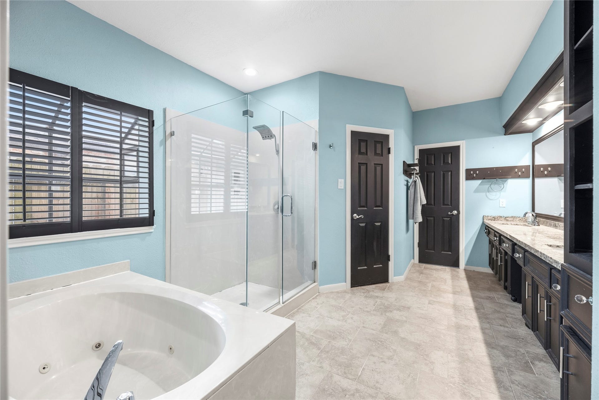 Spa-like primary bathroom is complete with a dual sink granite vanity, jetted tub, oversized frameless shower and a walk-in closet.