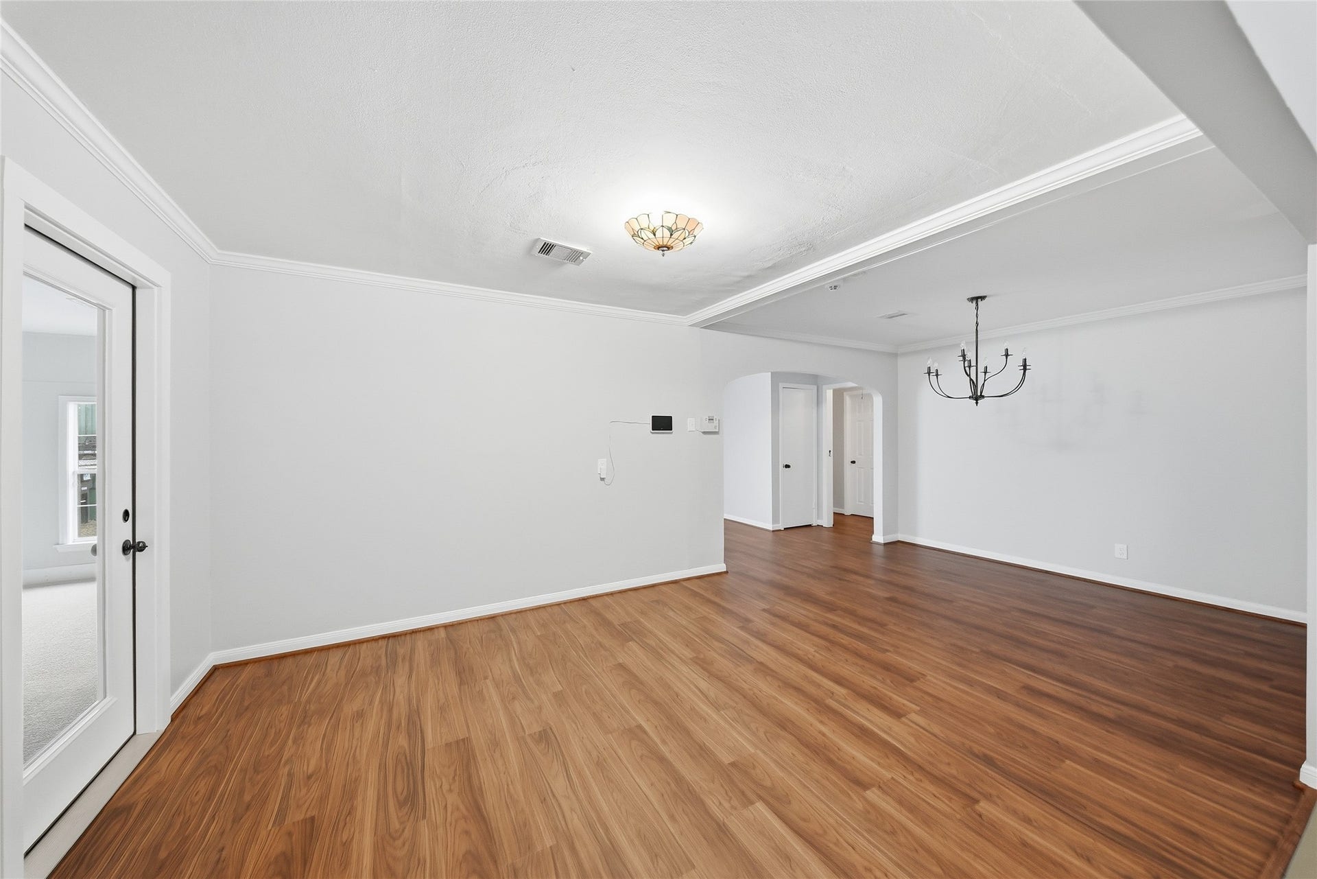Spacious living area with beautiful new flooring, crown molding, and a stylish chandelier, offering a seamless flow to the adjacent rooms.