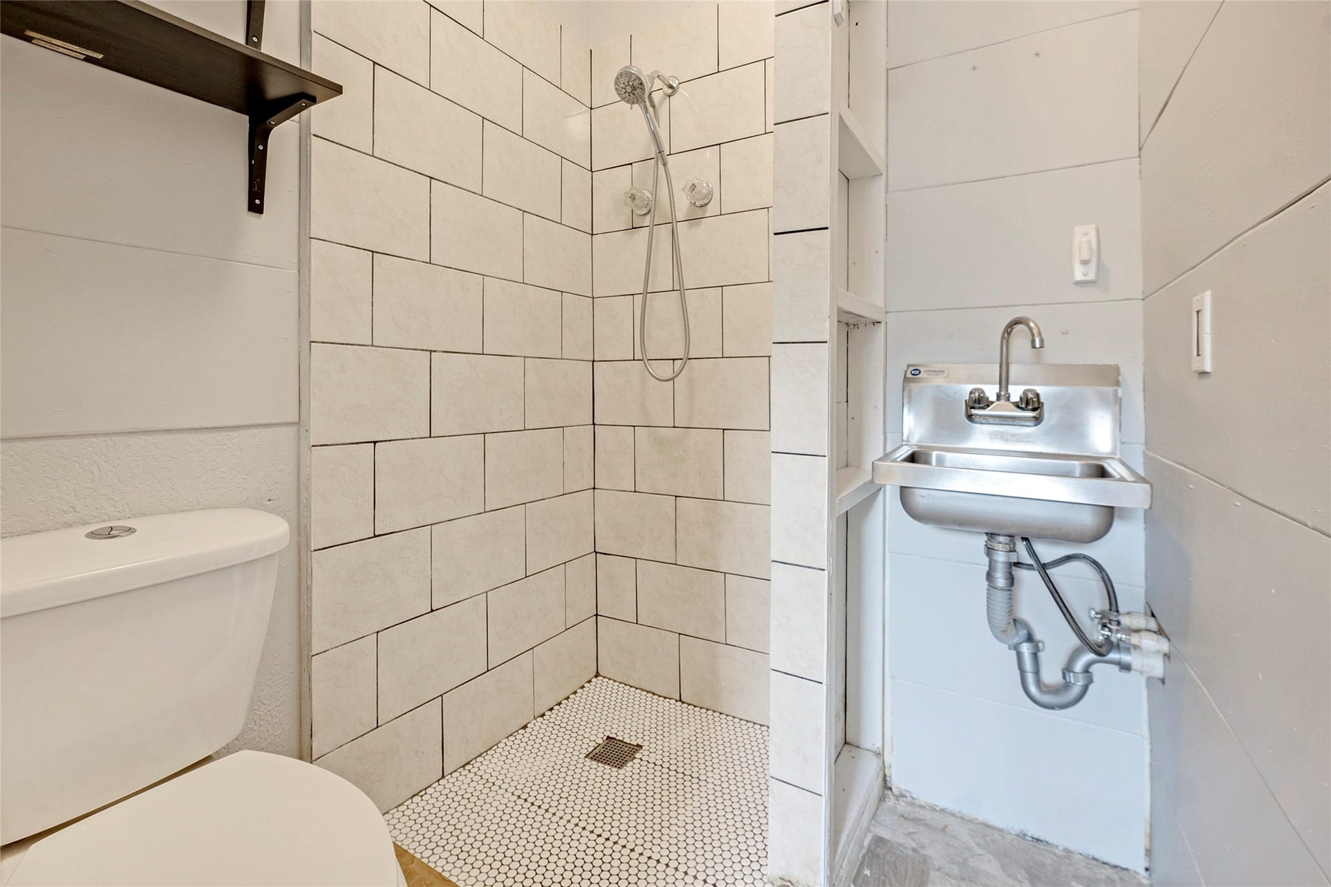 Compact bathroom featuring a modern tiled shower, efficient wall-mounted sink, and functional shelving for storage.