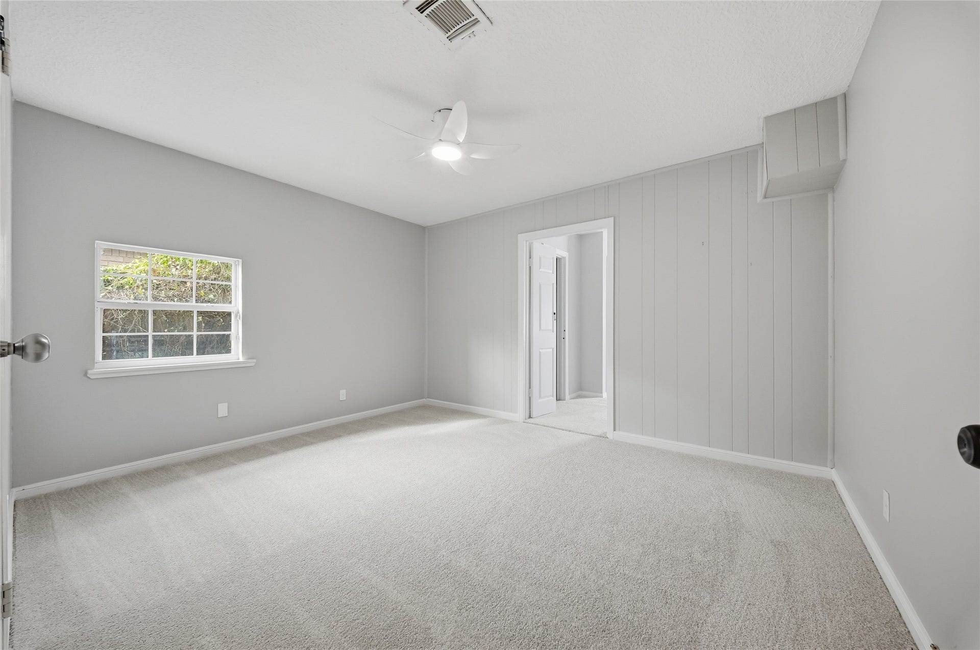 Spacious bedroom with soft carpeting, neutral gray walls and modern ceiling fan.