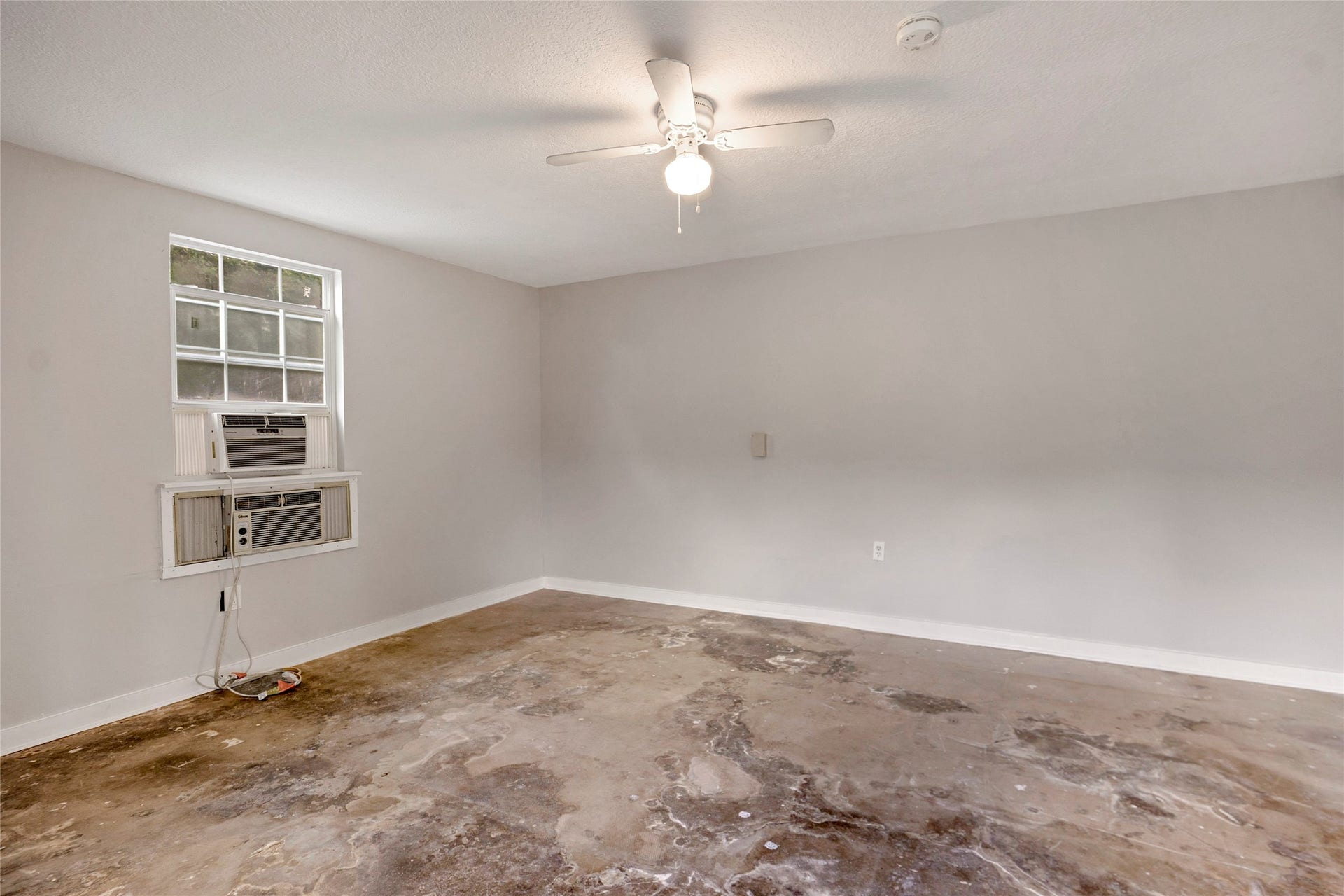 Spacious room with neutral walls, a ceiling fan, and a window air conditioning unit, offering potential for customization.