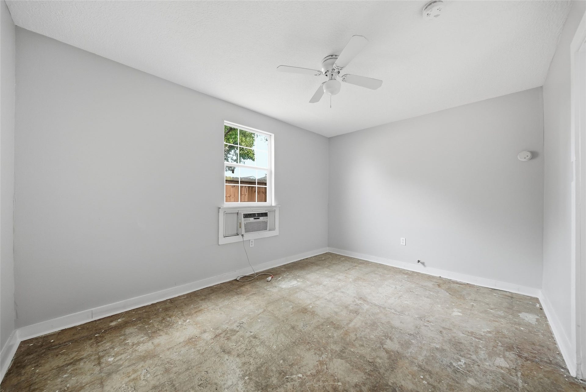 Bright room with neutral gray walls, a ceiling fan, and a window air conditioning unit, offering potential for customization.