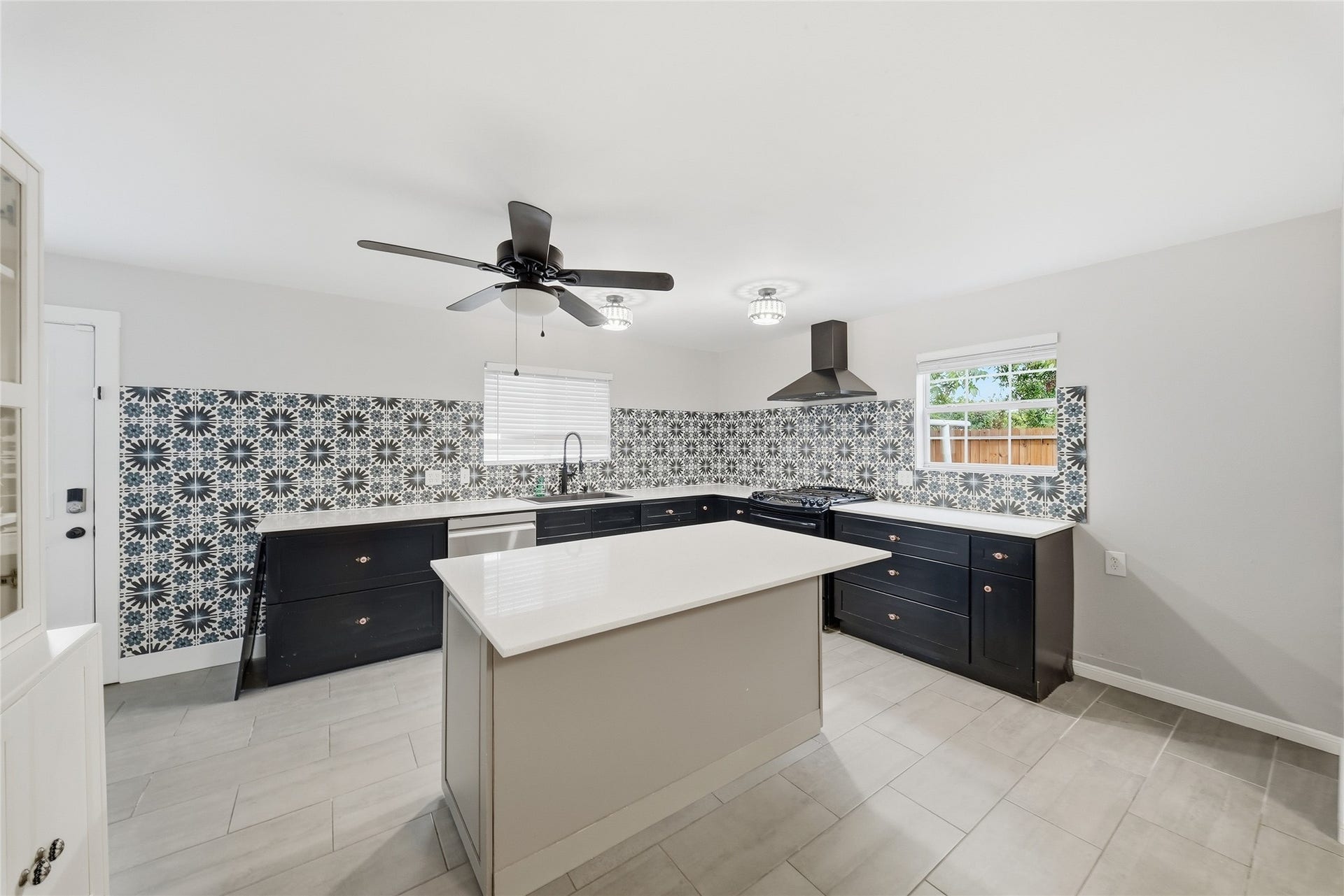 Open kitchen featuring a spacious island, sleek black cabinetry, and eye-catching patterned backsplash.